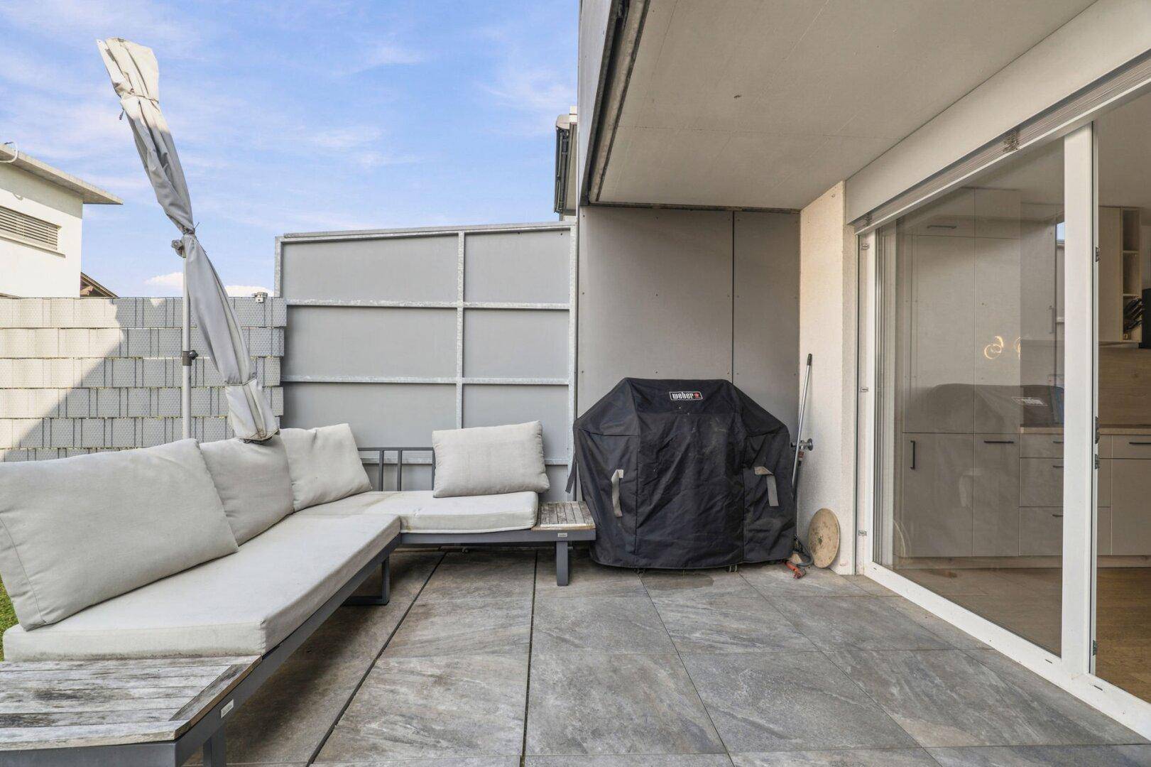 Sonniger Terrassenbereich mit Outdoor-Sofa und Grill, ideal für Entspannung.