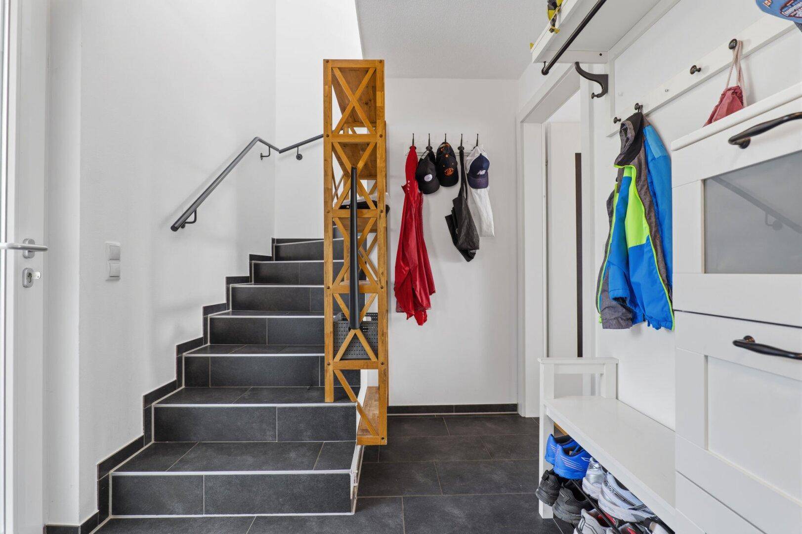 Eingangsbereich mit Treppe, dunklen Fliesen und Garderobe.