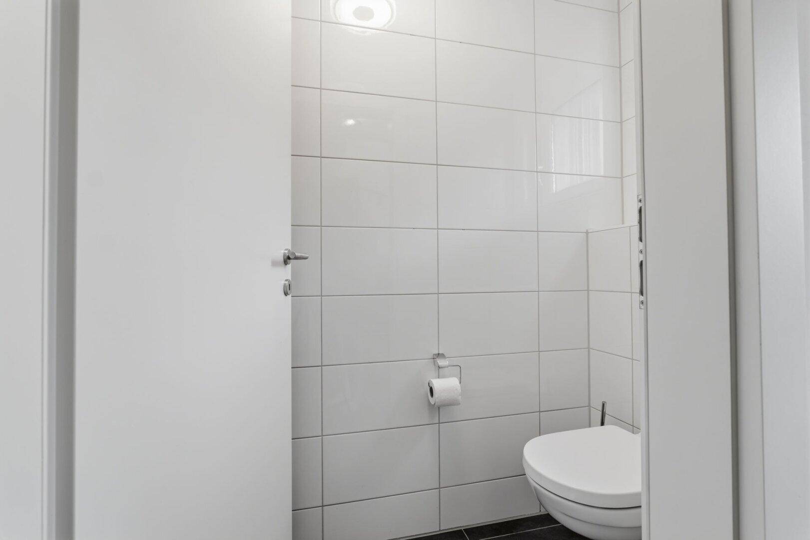 Kleines Gäste-WC mit weißen Fliesen und wandhängendem WC.
