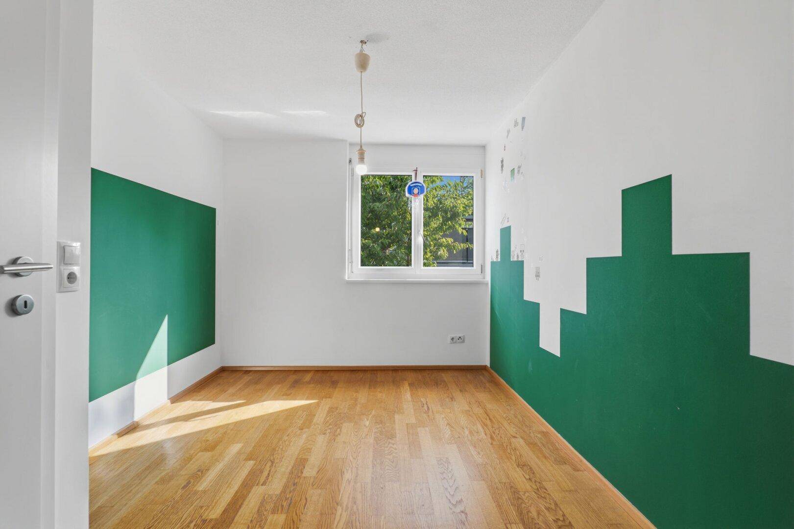 Helles Zimmer mit Holzboden und kreativer grün-weißer Wandgestaltung.