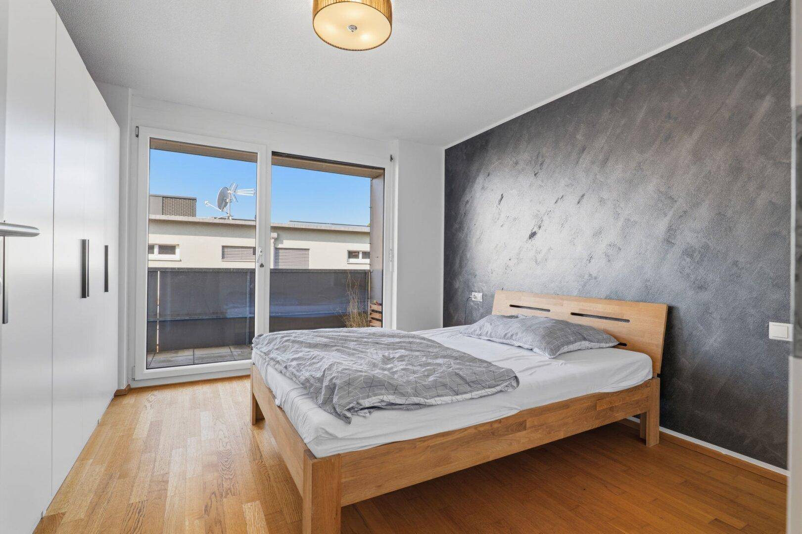 Schlafzimmer mit Holzbett, Kleiderschrank und direktem Zugang zum Balkon.