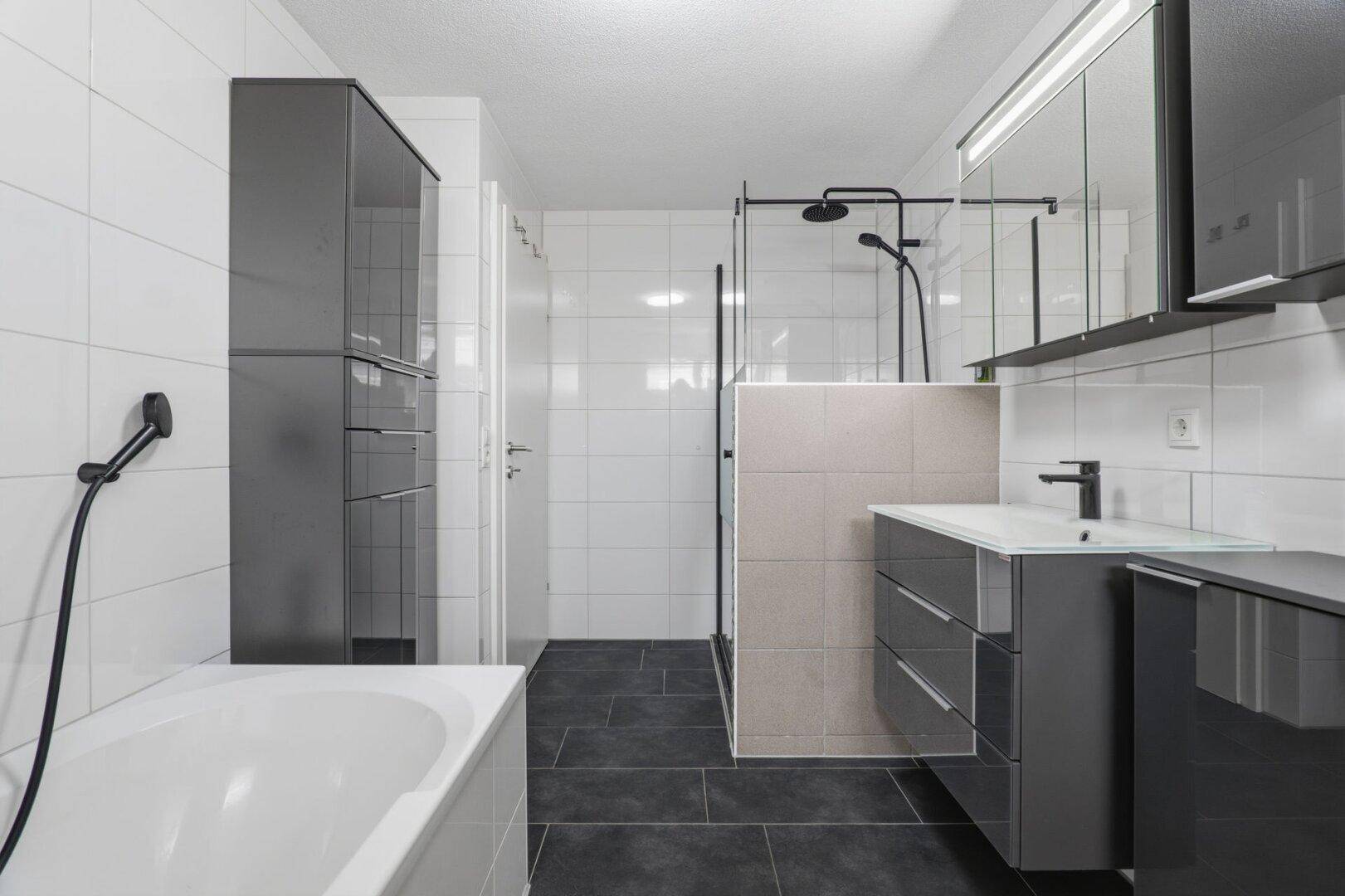 Modernes Badezimmer mit Dusche, Badewanne und dunklen Bodenfliesen.