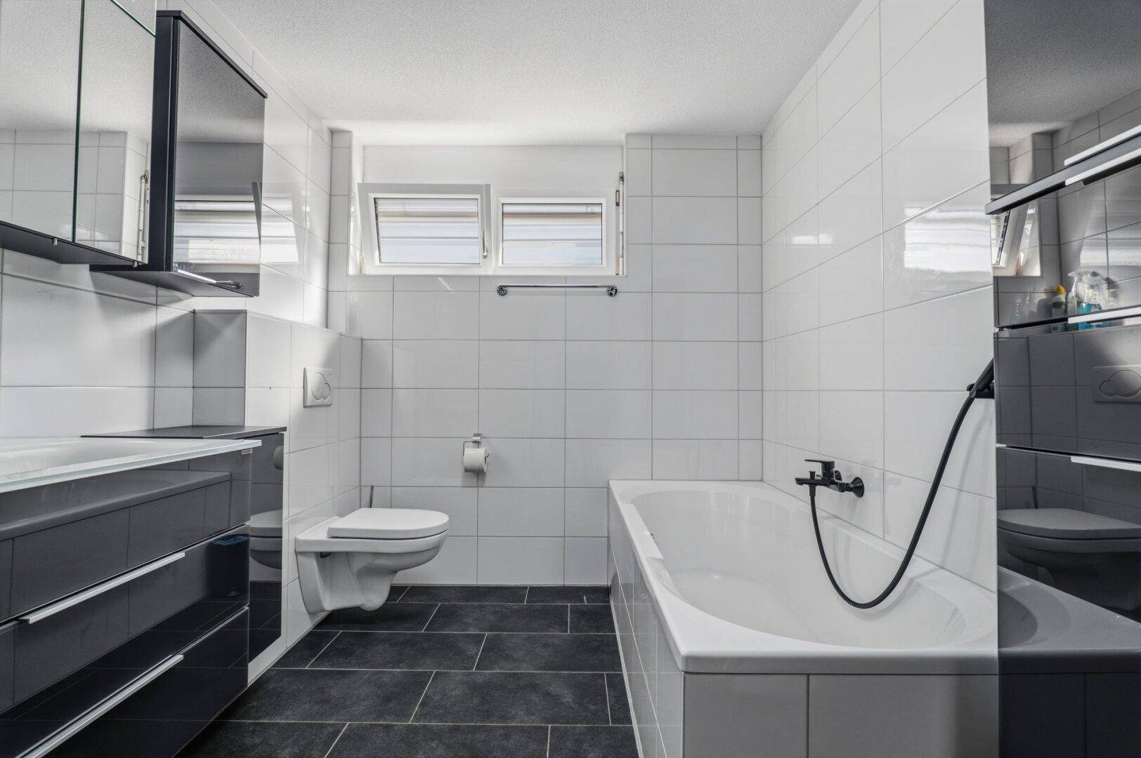 Modernes Badezimmer mit Badewanne, WC und weißen Fliesen.