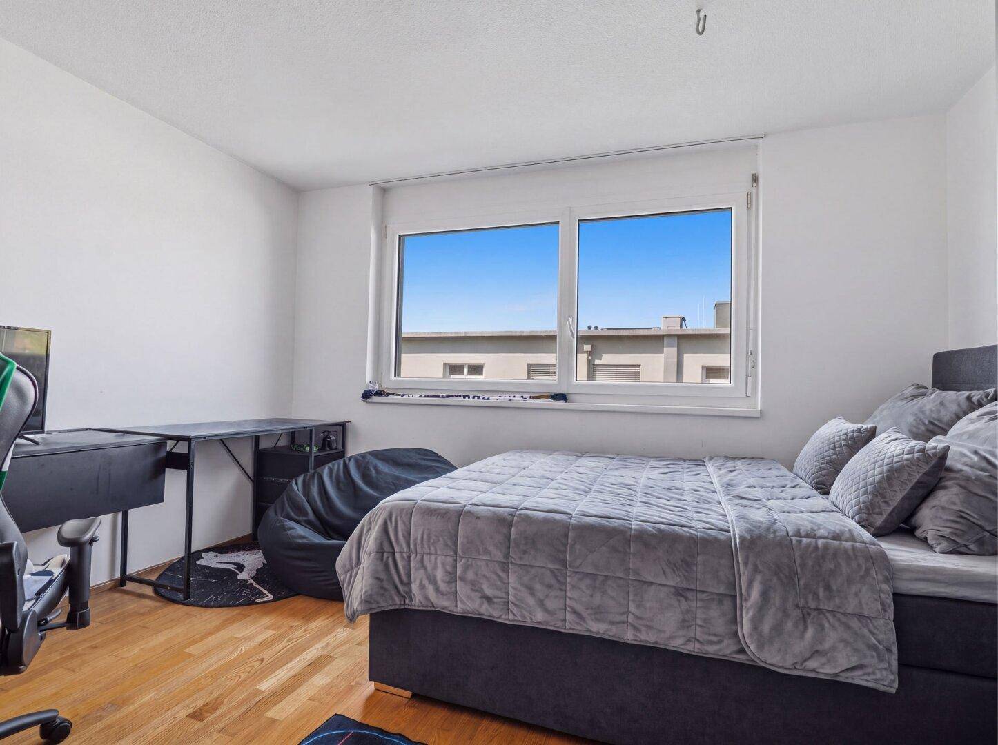 Schlafzimmer mit Holzboden, großem Fenster und modernem Bett.