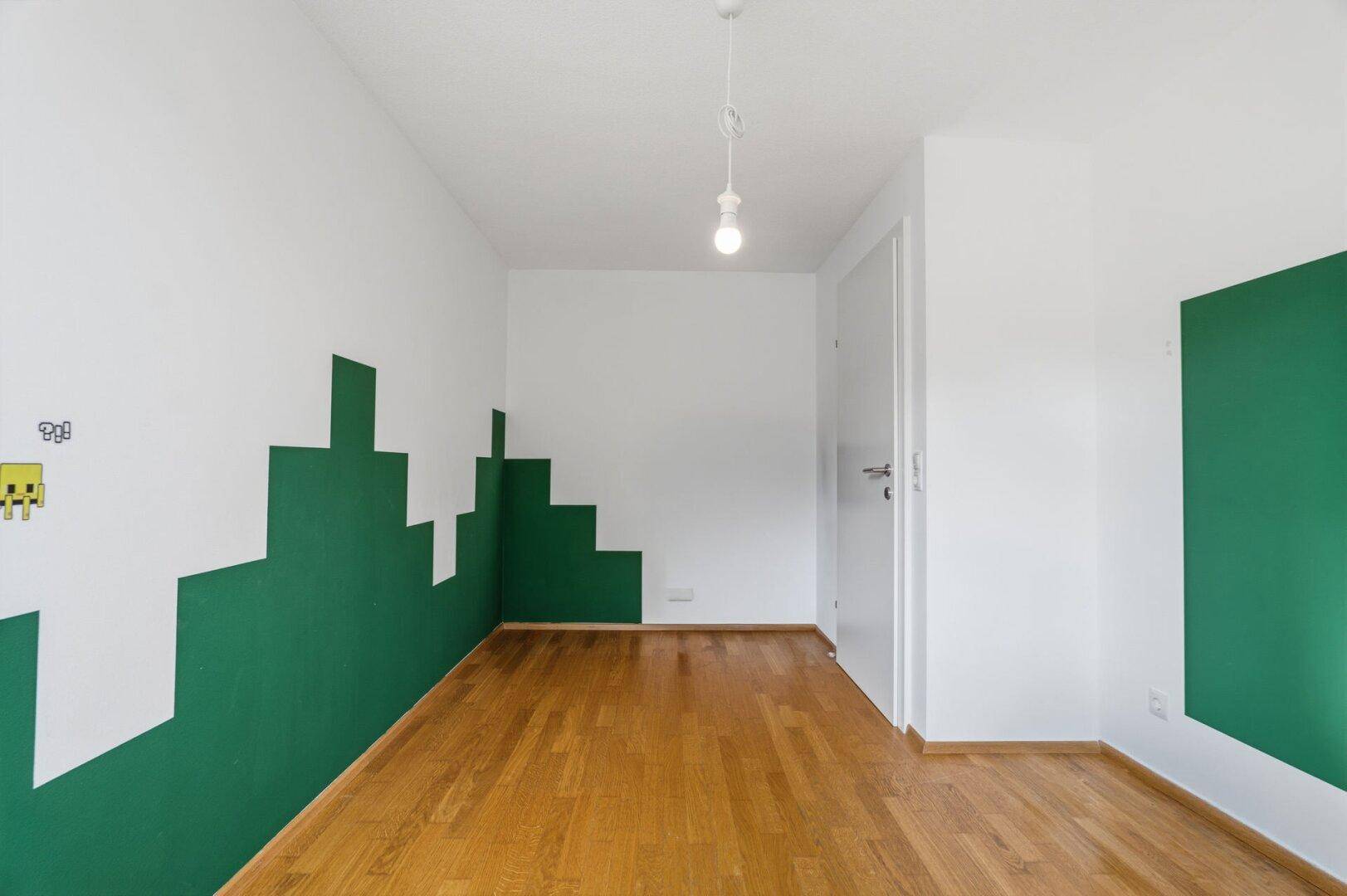 Kinderzimmer mit Holzboden und spielerischer Wandgestaltung in Grün und Weiß.