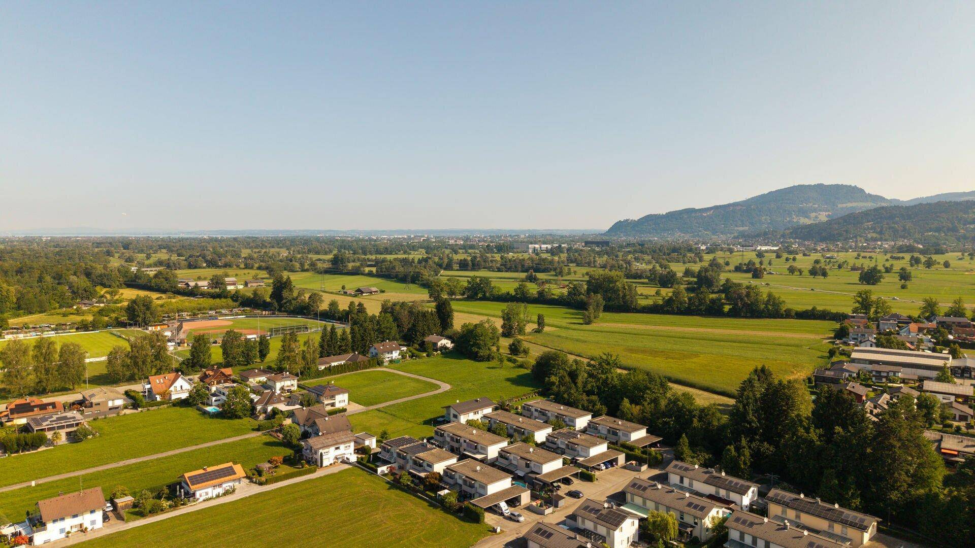 Ausgedehnte Landschaftsaufnahme einer Wohnsiedlung mit Feldern und Wäldern im Hintergrund.