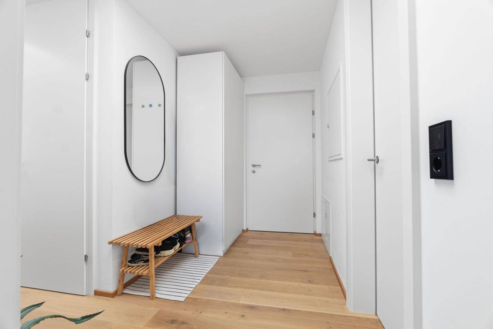Heller Eingangsbereich mit Holzboden, Garderobe und modernem Spiegel.