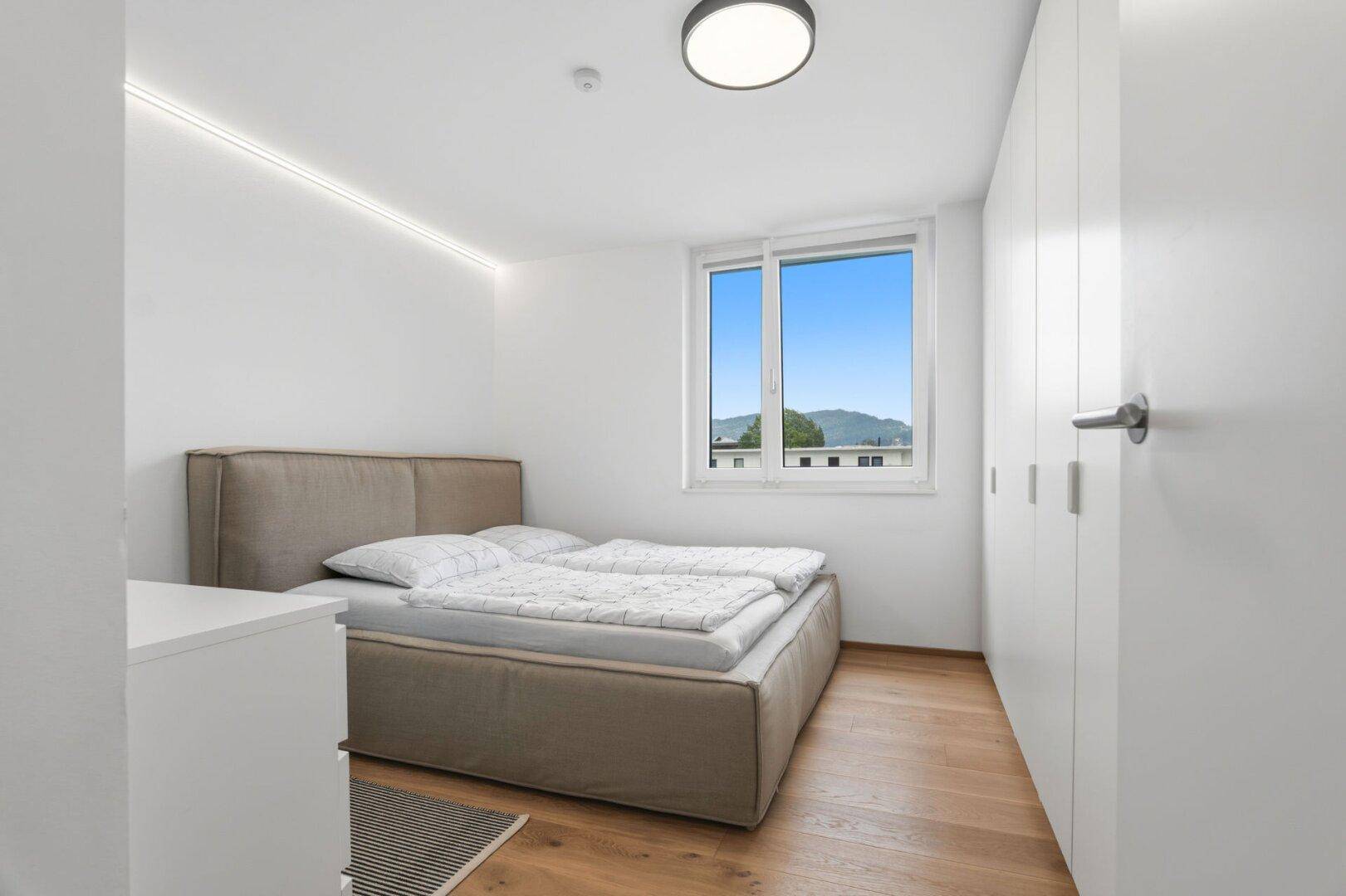 Gemütliches Schlafzimmer mit Holzboden, großem Fenster und Blick auf die Umgebung.