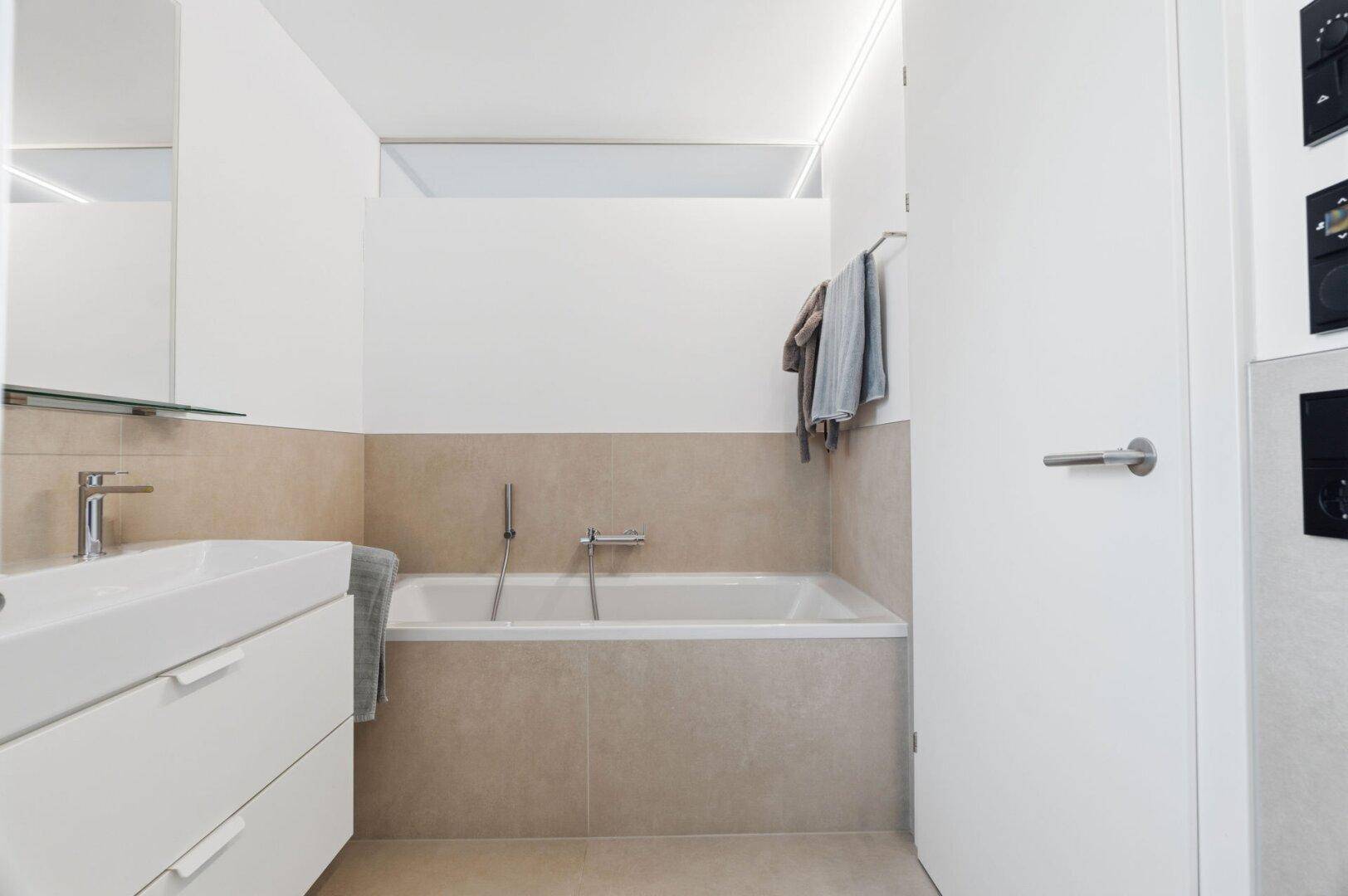 Helles Badezimmer mit Badewanne, modernem Waschtisch und indirekter Beleuchtung.