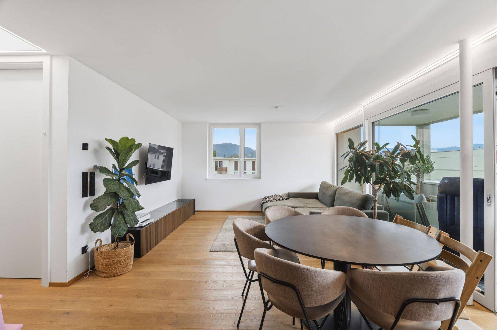 Geräumiges Wohnzimmer mit Holzboden, großem Fenster und Zugang zum Balkon.