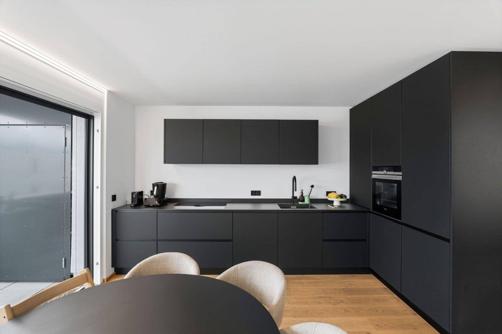 Elegante schwarze Einbauküche mit modernen Geräten und Essbereich im offenen Wohnkonzept.