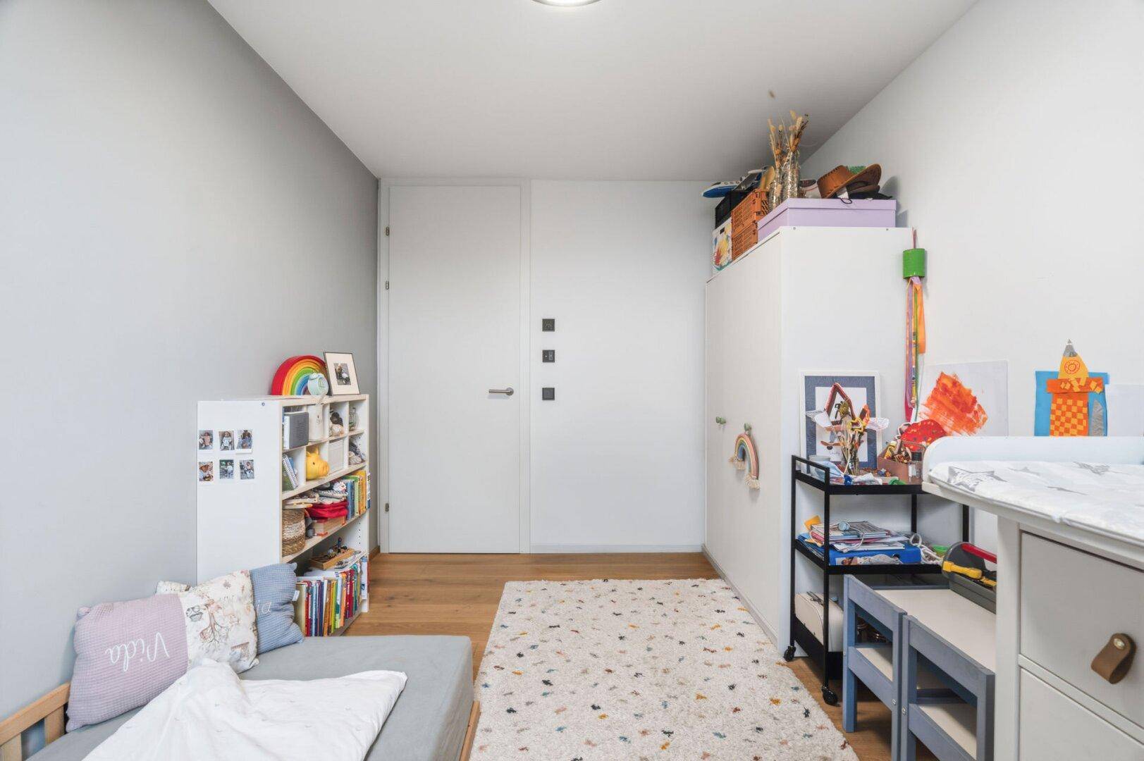 Freundliches Kinderzimmer mit Holzboden, Spielzeug und heller Einrichtung.