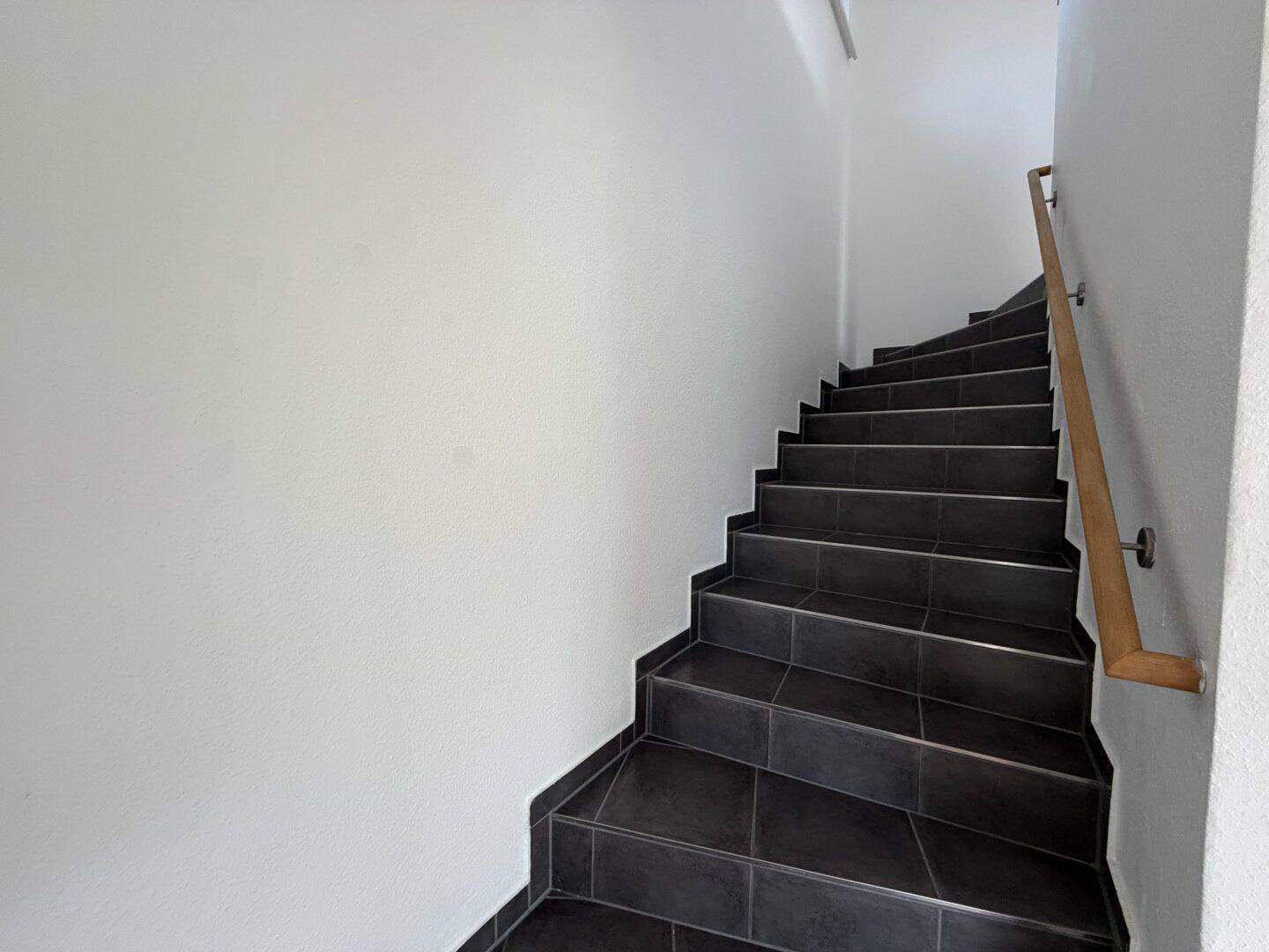 Treppenhaus mit dunklen Fliesenstufen und einem schlichten Holzgeländer.