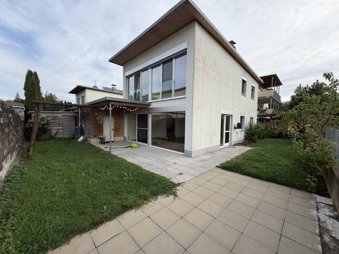 Modernes Einfamilienhaus mit Flachdach, großen Fenstern, Terrasse und Garten.