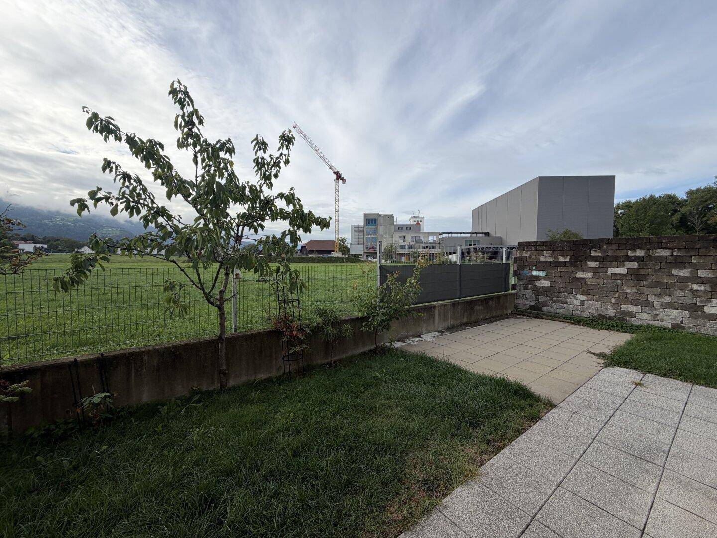 Außenbereich mit gepflasterter Terrasse, Rasenfläche und weitem Blick ins Grüne.