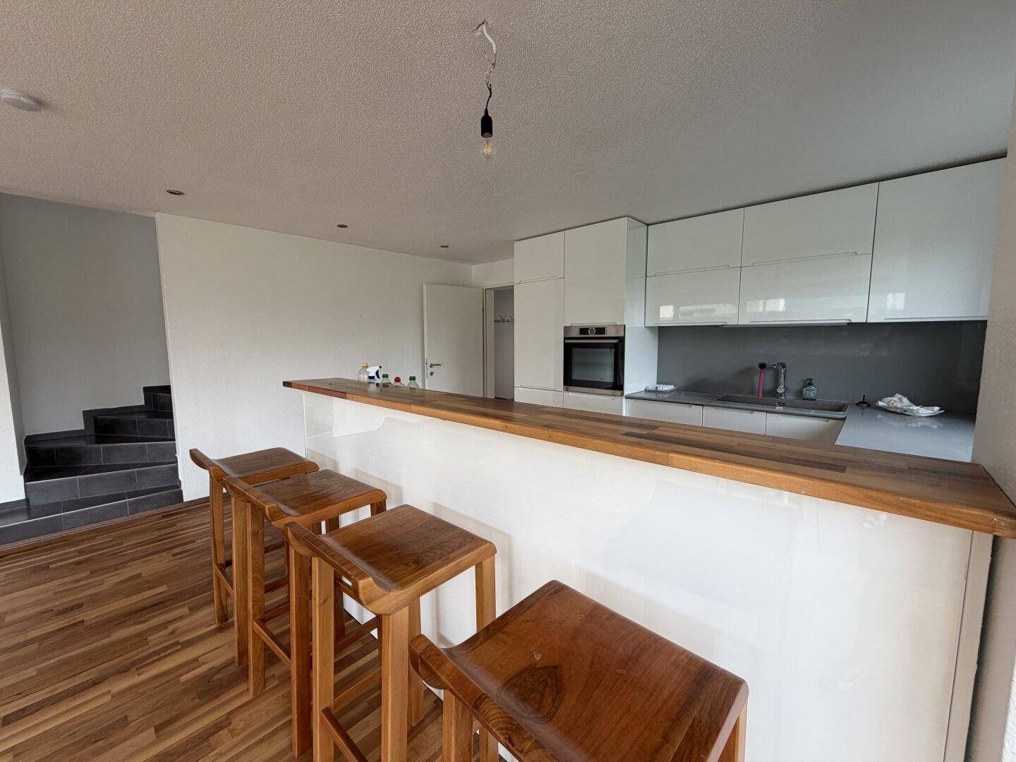 Offener Wohnbereich mit Küche, Frühstücksbar und Treppe, ausgestattet mit Holzboden.