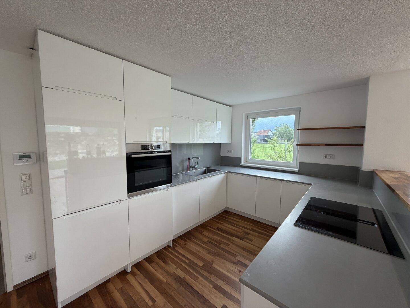 Moderne Einbauküche mit weißen Hochglanzschränken, Induktionskochfeld und Blick ins Grüne.