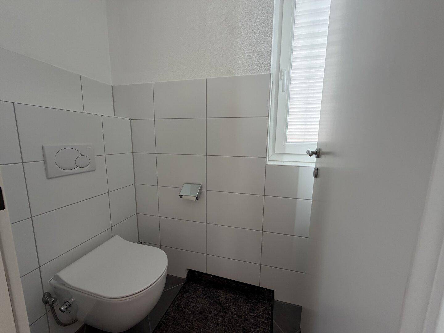 Modernes Gäste-WC mit Wand-WC und Fenster, ausgestattet mit hellen Fliesen.