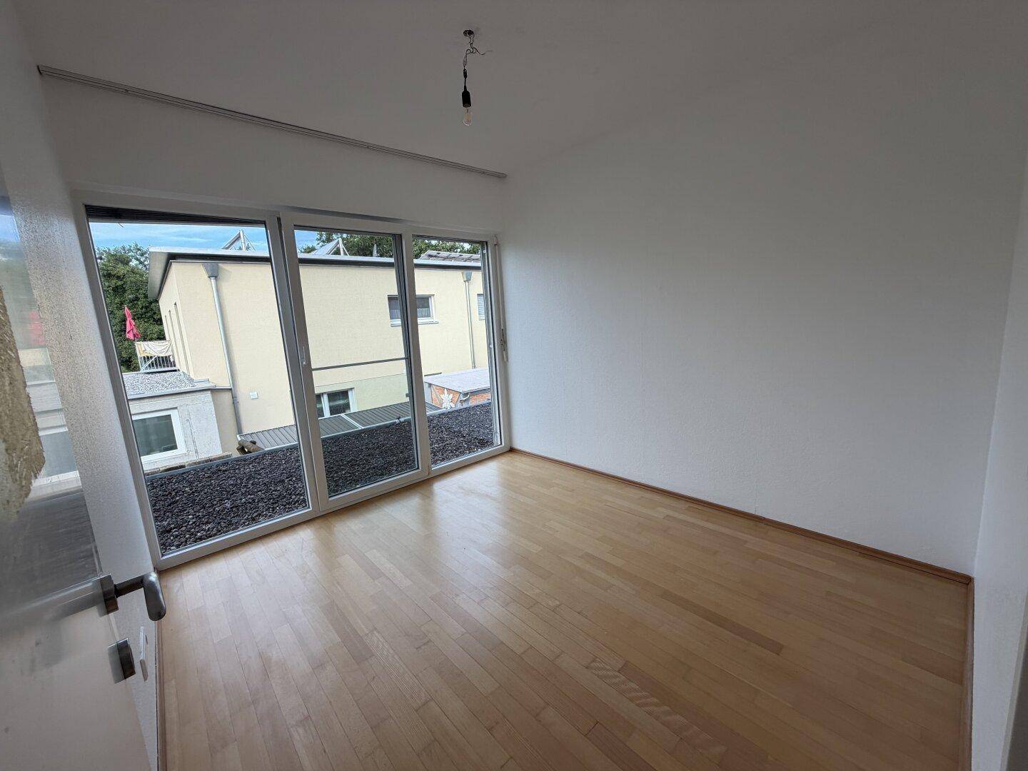 Helles Zimmer mit Holzboden und großen Schiebetüren zu einem Außenbereich.