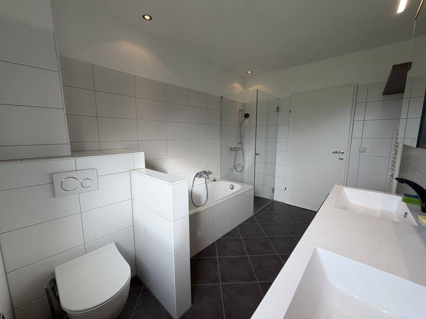 Modernes Badezimmer mit Badewanne, begehbarer Dusche und Wand-WC in hellen Fliesen.