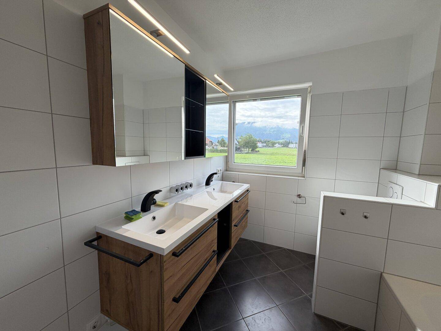 Modernes Badezimmer mit Doppelwaschbecken, Spiegelschrank und Fenster mit Blick ins Grüne.