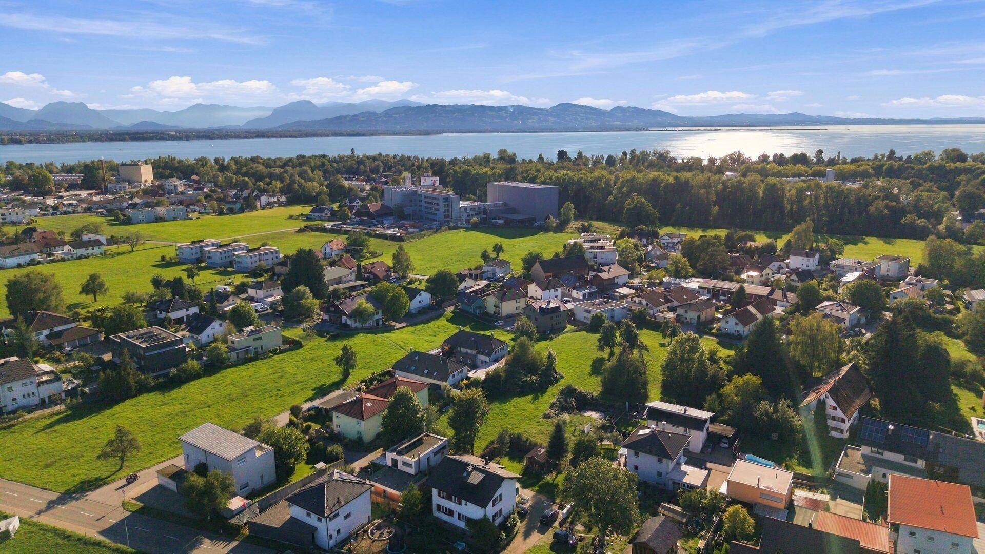 Luftaufnahme eines Wohngebiets mit weitem Blick auf einen See und die umliegende Berglandschaft.