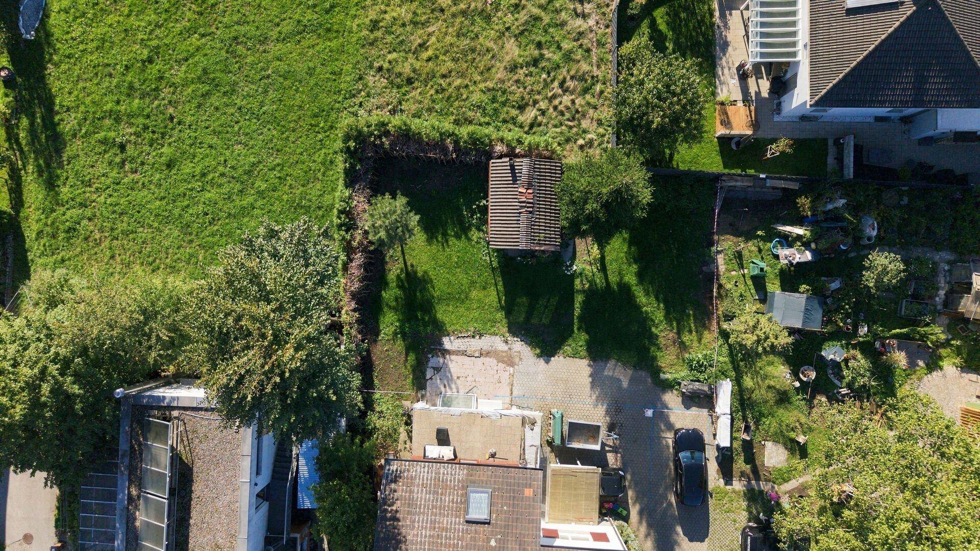 Senkrechte Luftaufnahme eines Gartengrundstücks mit Rasenfläche, Schuppen und angrenzenden Gebäuden.