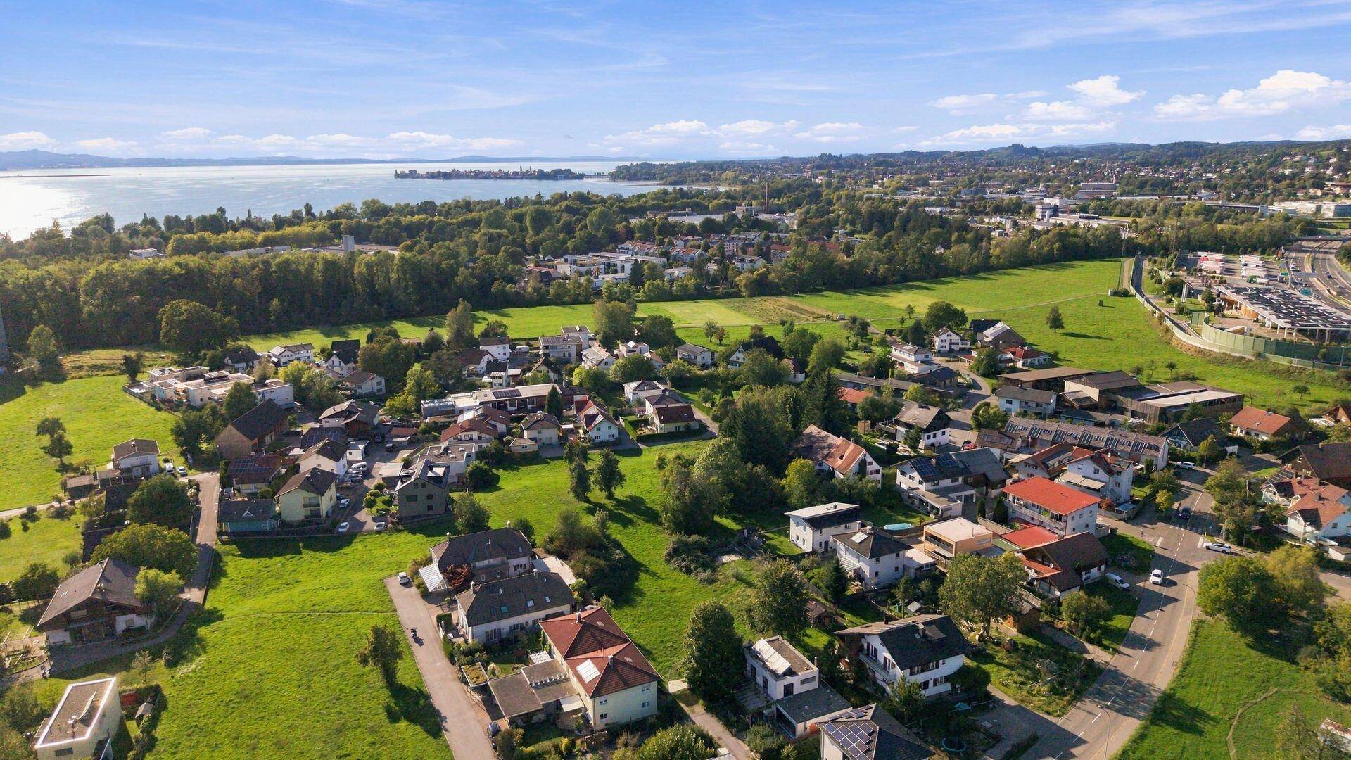 Luftaufnahme einer Wohnsiedlung mit weiten Grünflächen und einem See am Horizont.
