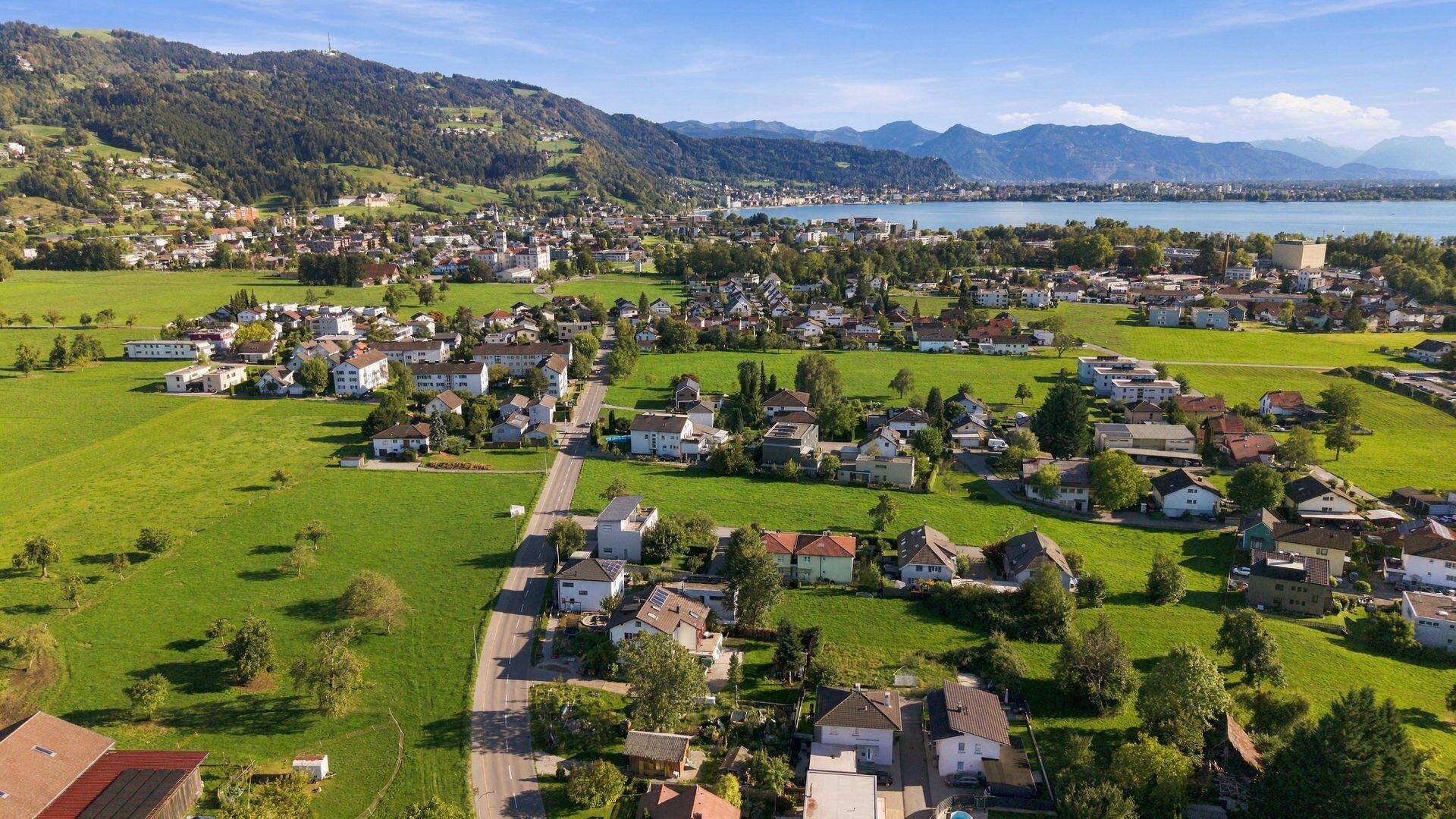 Luftaufnahme einer Wohnsiedlung mit Blick auf den See und die dahinterliegende Bergkette.