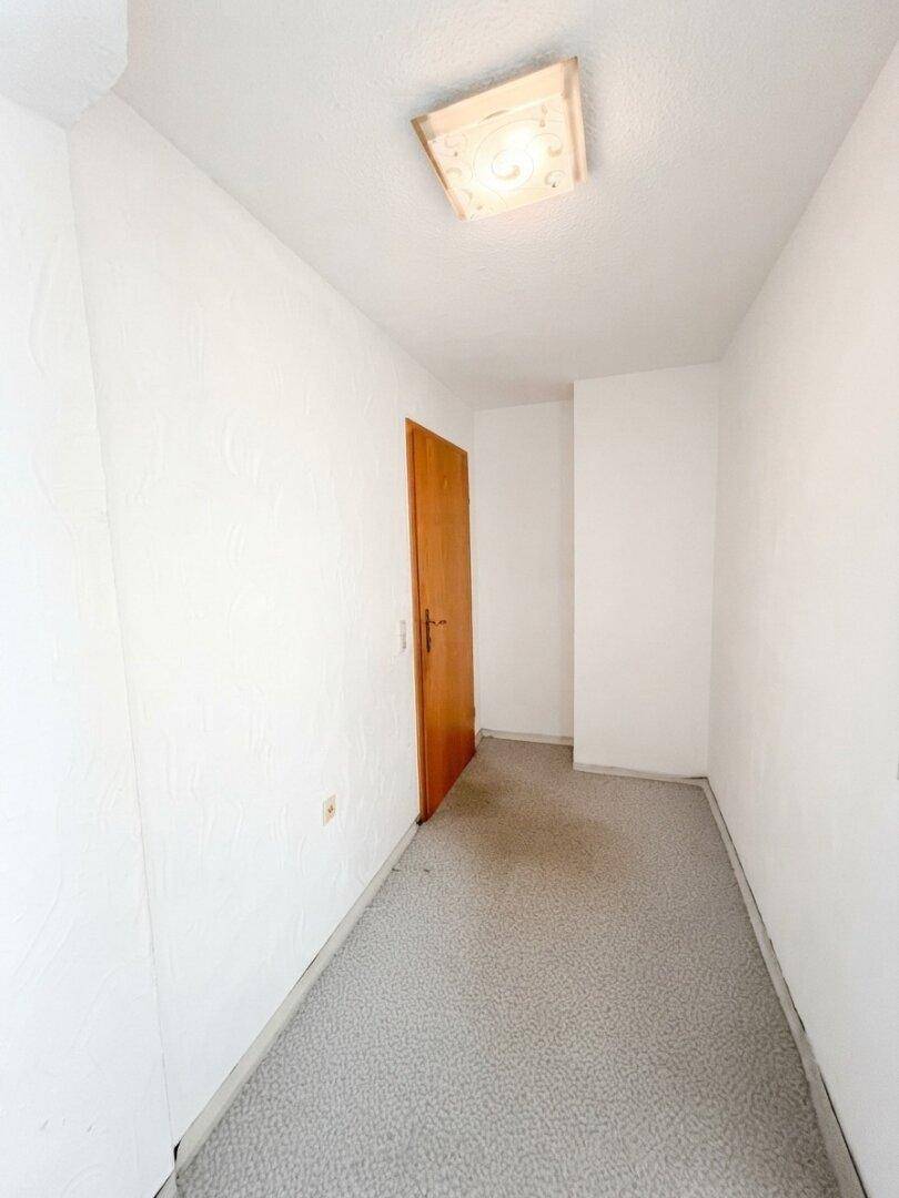 Schmaler Flur mit Teppichboden und einer Holztür, die zu weiteren Räumen führt.