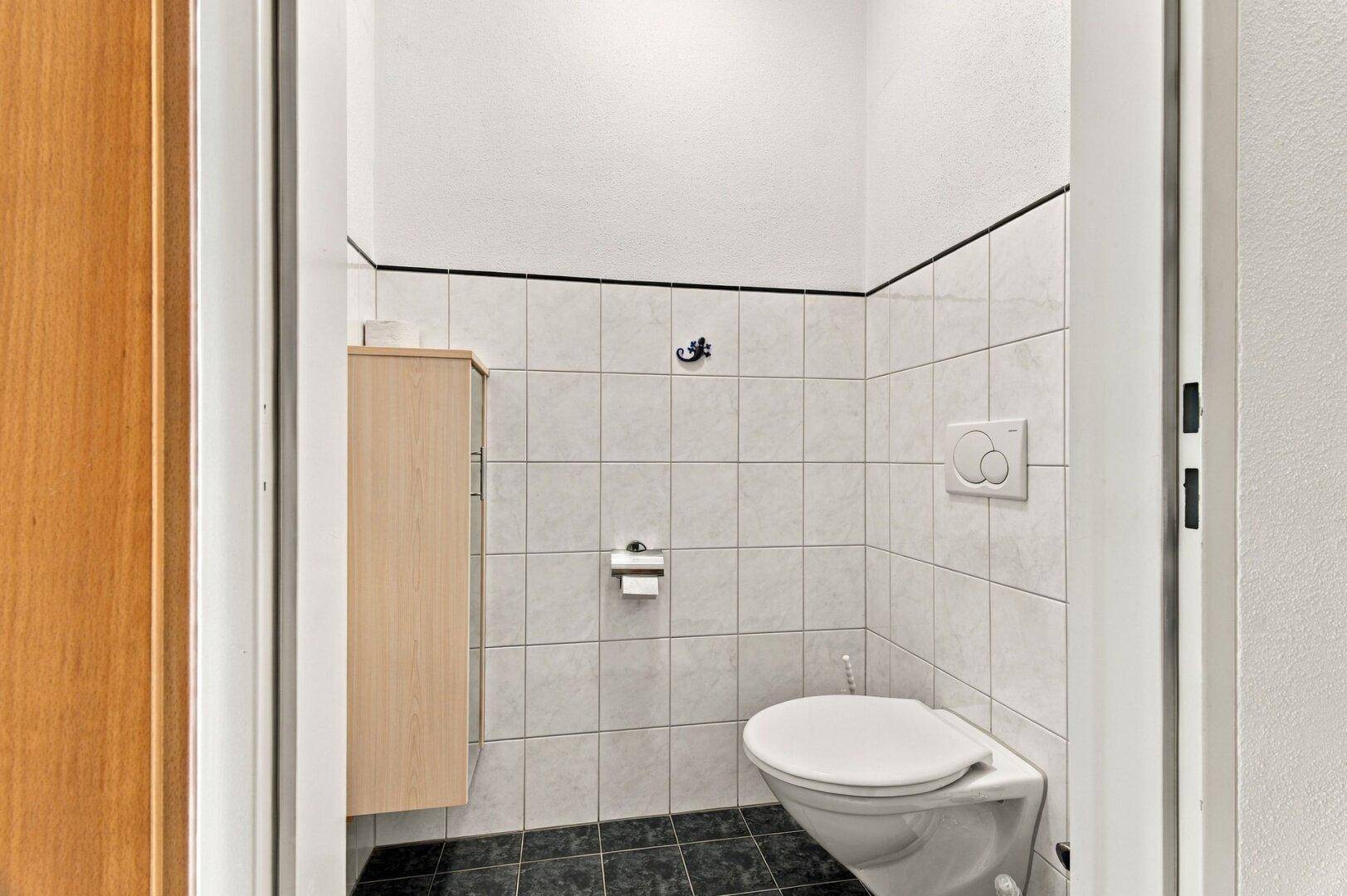 Separates WC mit wandhängender Toilette und kleinem Schrank.