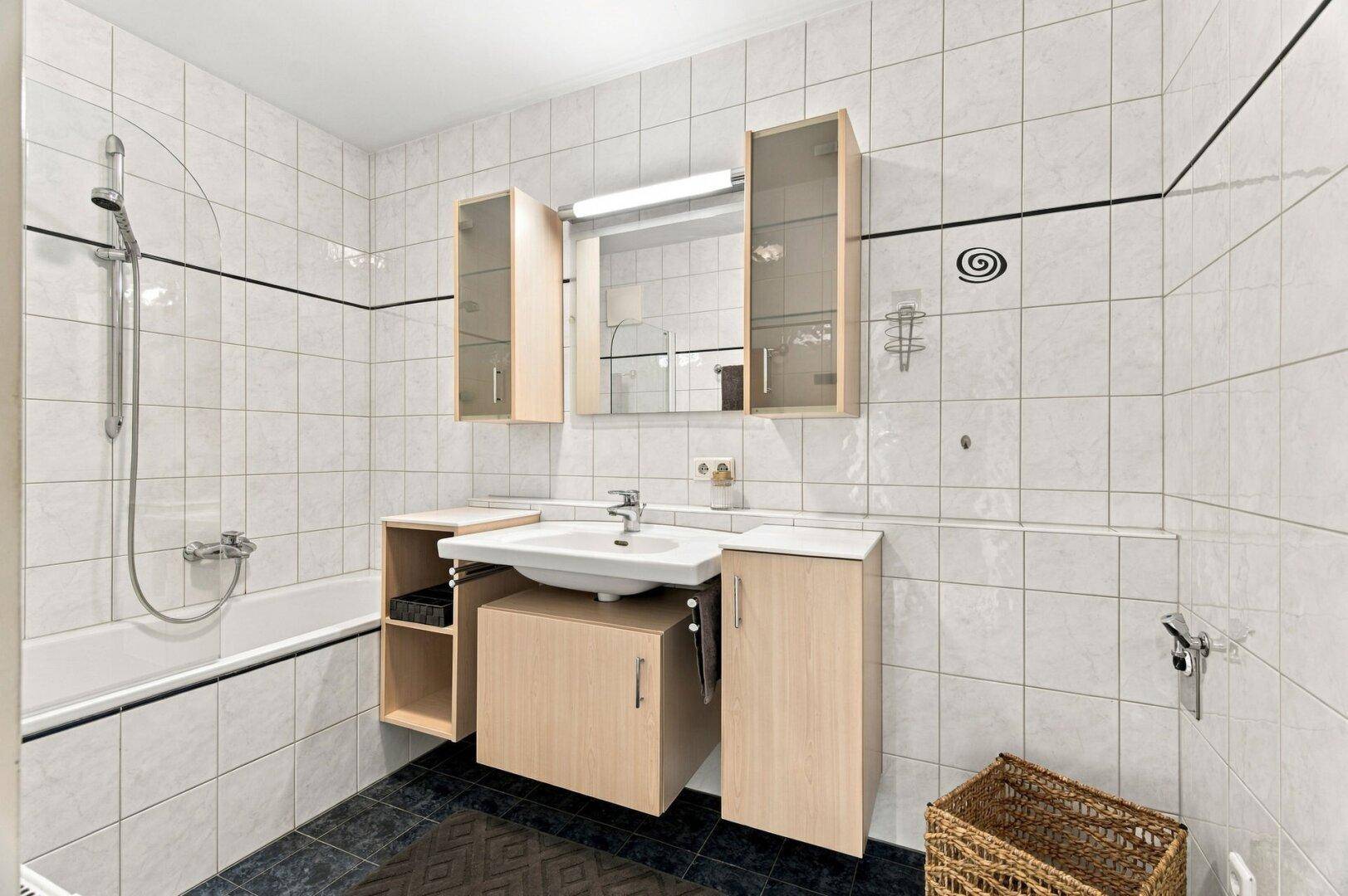 Badezimmer mit Badewanne, Duschfunktion, Waschbecken und Spiegelschrank.