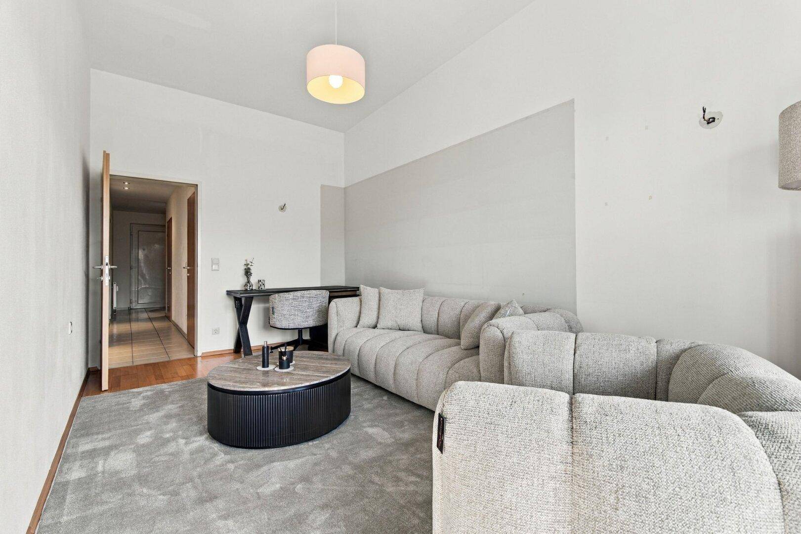 Gemütliches Wohnzimmer mit modernem Sofa, Teppich und einem kleinen Arbeitsbereich.