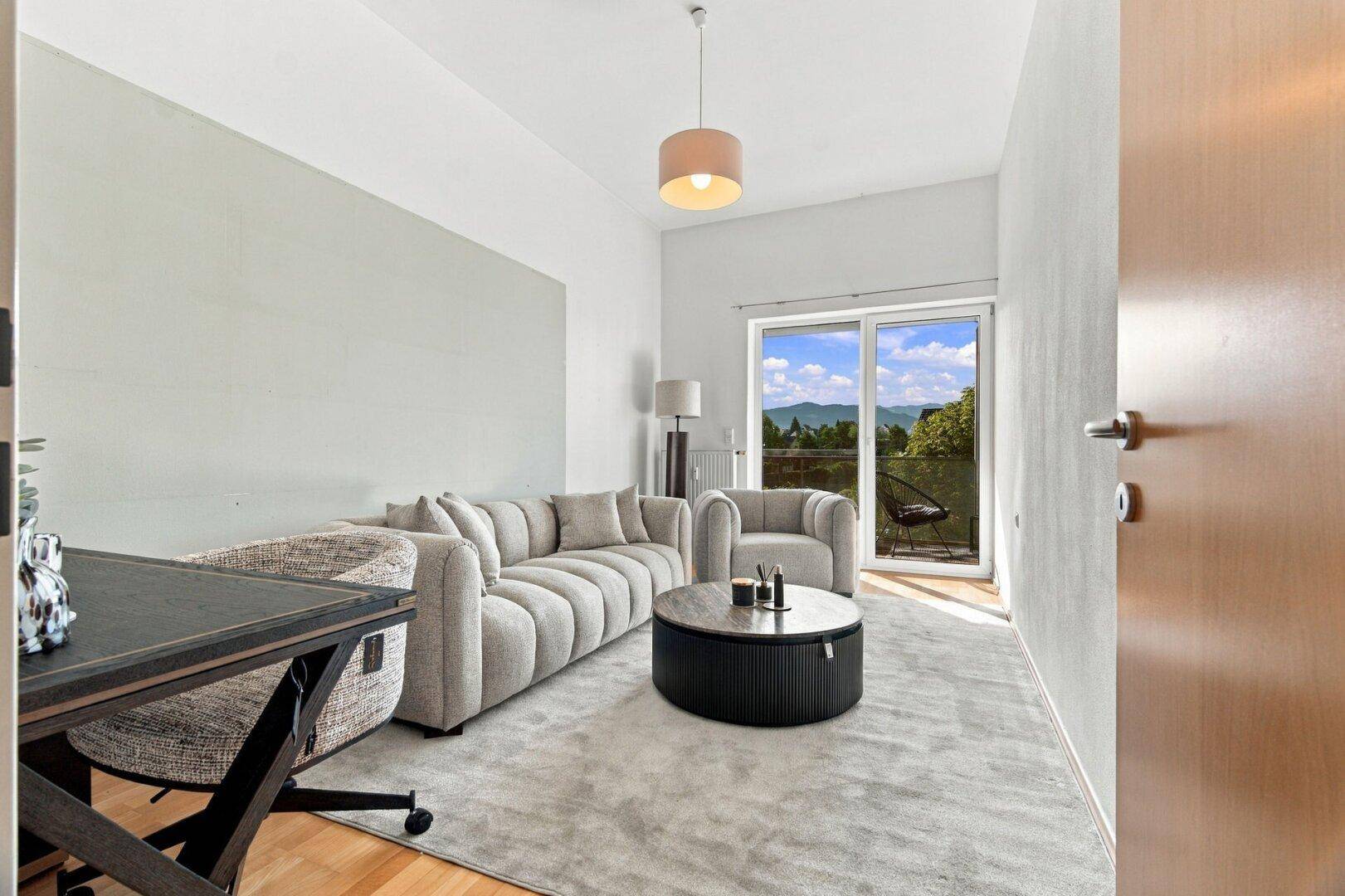 Modernes Wohnzimmer mit beigem Sofa, Teppichboden und Zugang zum Balkon mit schöner Aussicht.