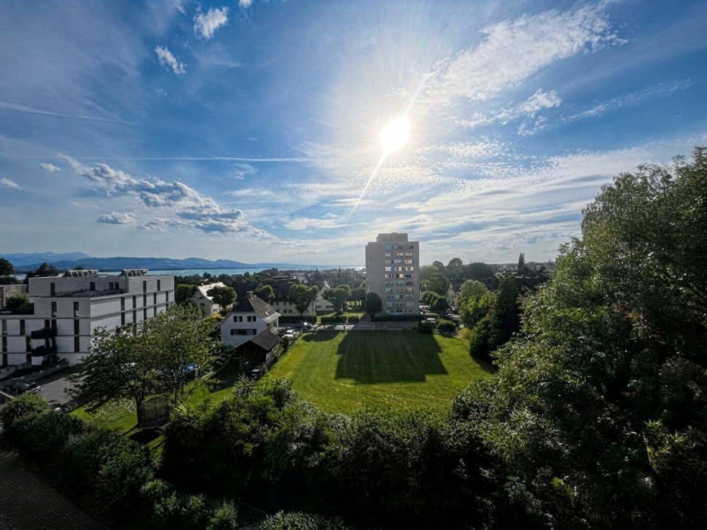 Weitläufiger Blick über die Stadt mit See im Hintergrund und sonnigem Himmel.
