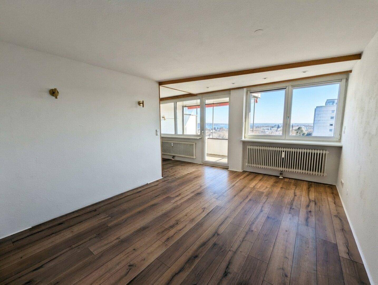 Helles Wohnzimmer mit Laminatboden, großen Fenstern und Zugang zum Balkon.