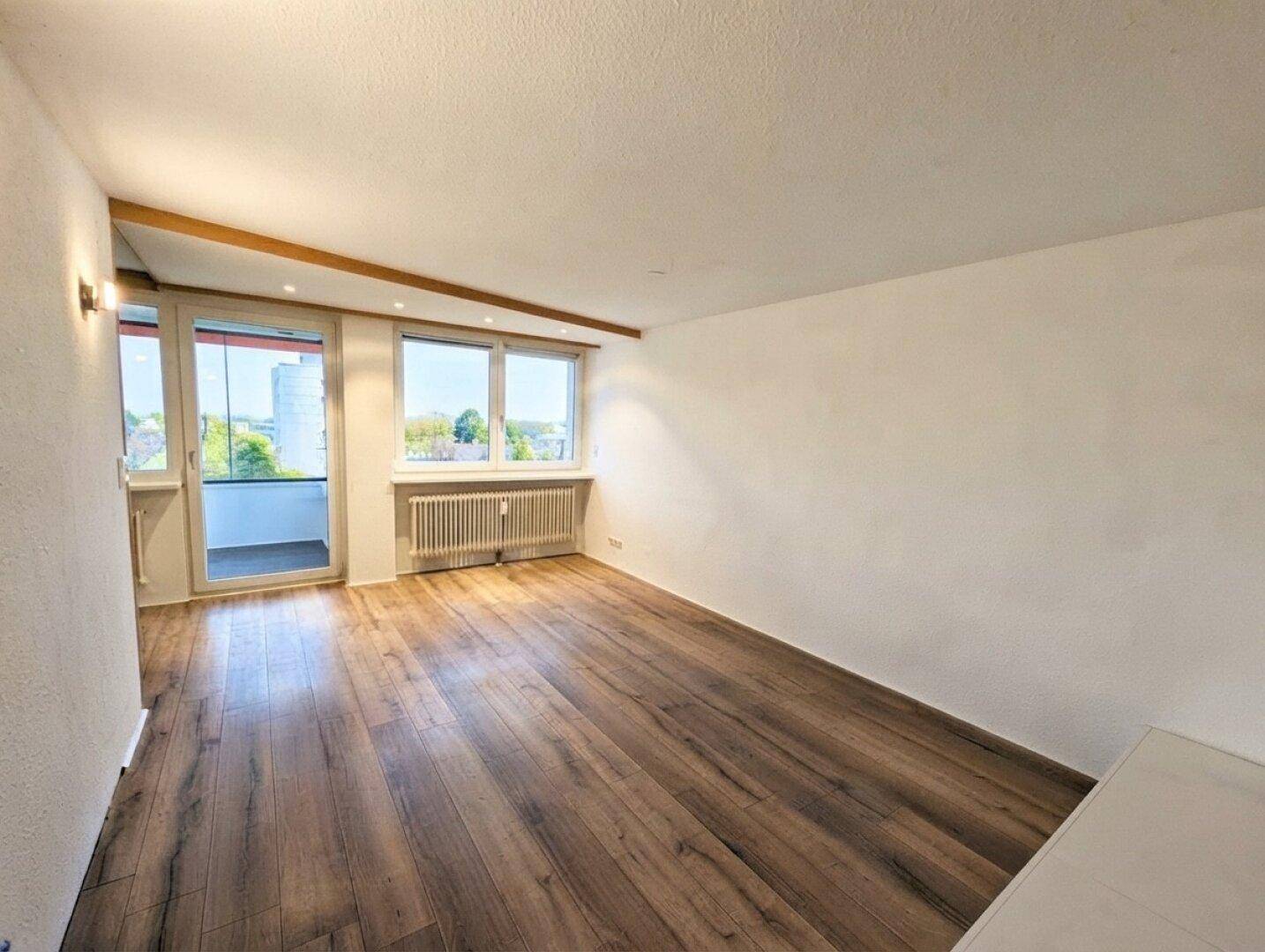 Geräumiges Wohnzimmer mit Laminatboden, hellen Wänden und viel Tageslicht.
