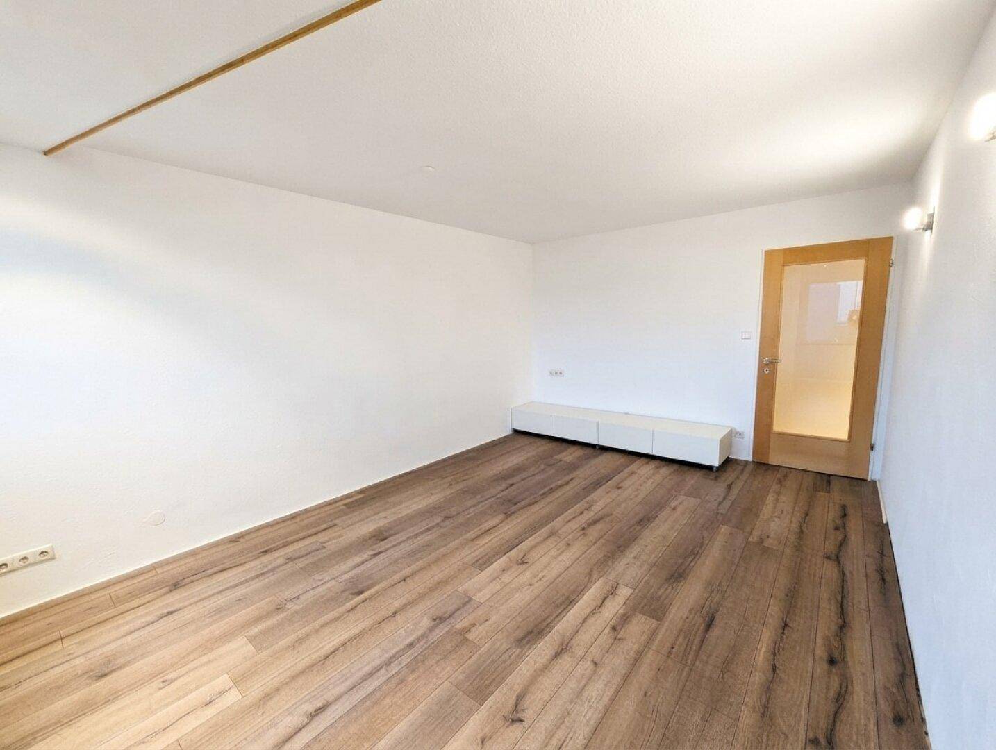 Heller Wohnbereich mit Laminatboden und einer modernen, niedrigen Kommode.