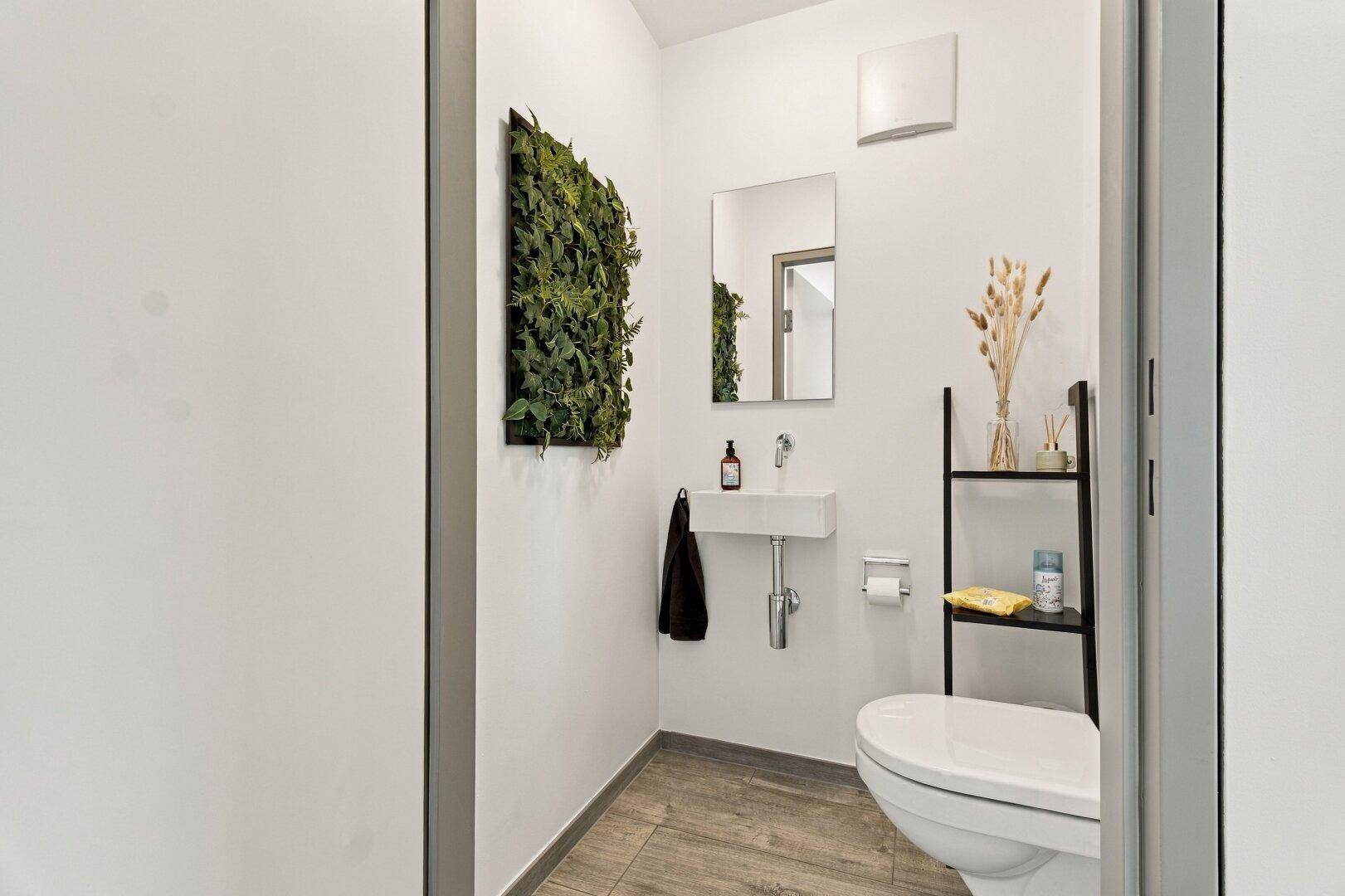 Modernes Gäste-WC mit kleinem Waschbecken, Toilette und dekorativer Pflanzenwand.