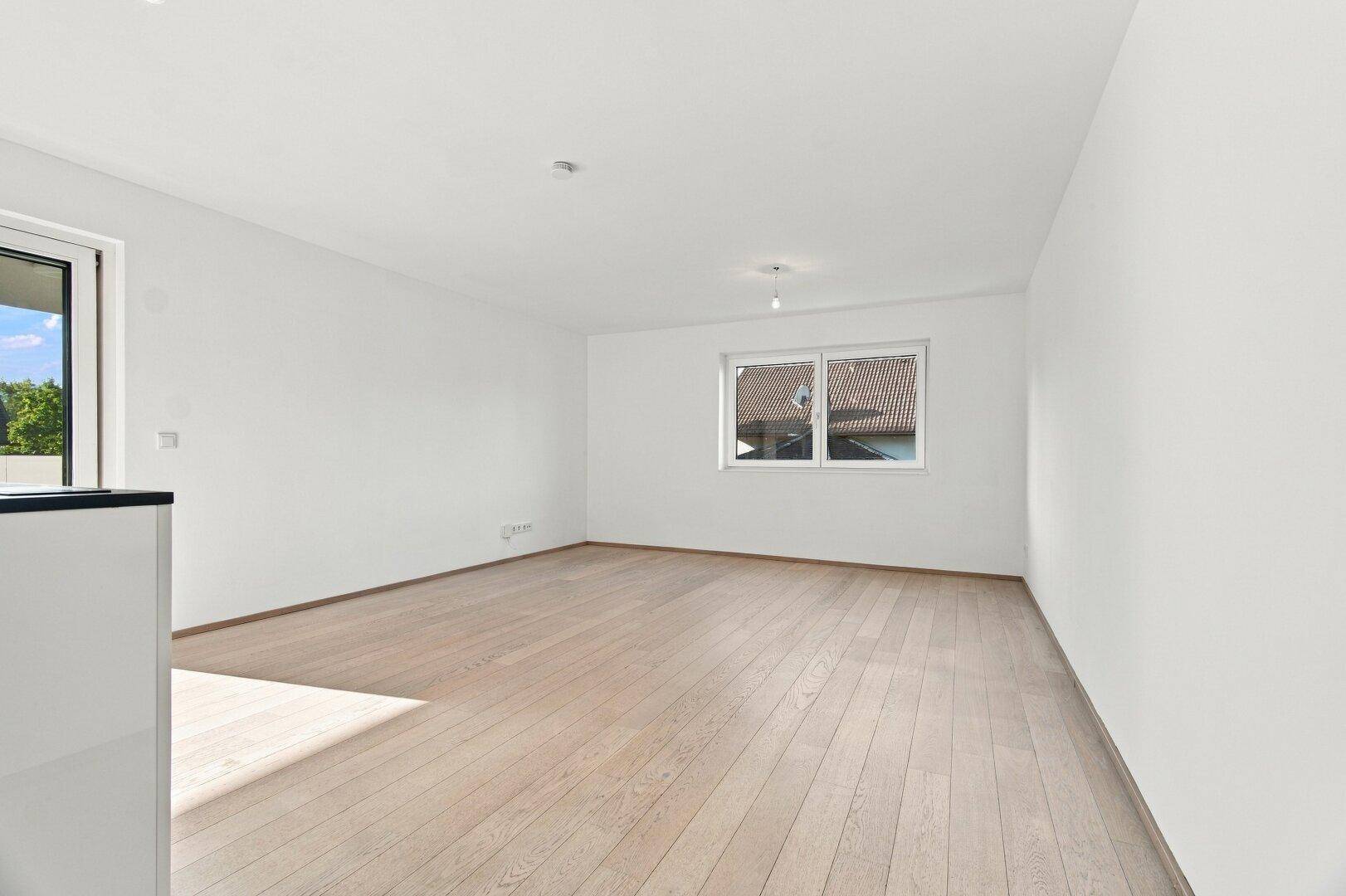 Geräumiges, unmöbliertes Wohnzimmer mit hellem Holzboden und großem Fenster.