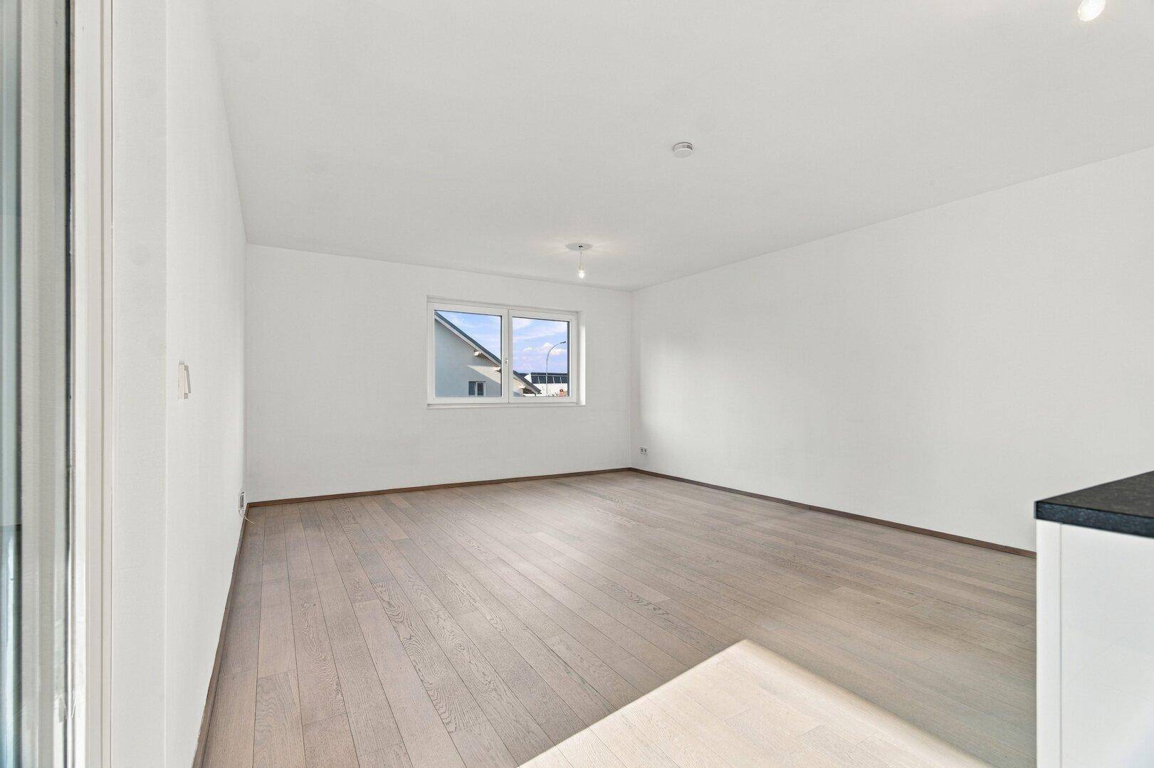 Helles, unmöbliertes Wohnzimmer mit Holzboden und Zugang zu einem Außenbereich.