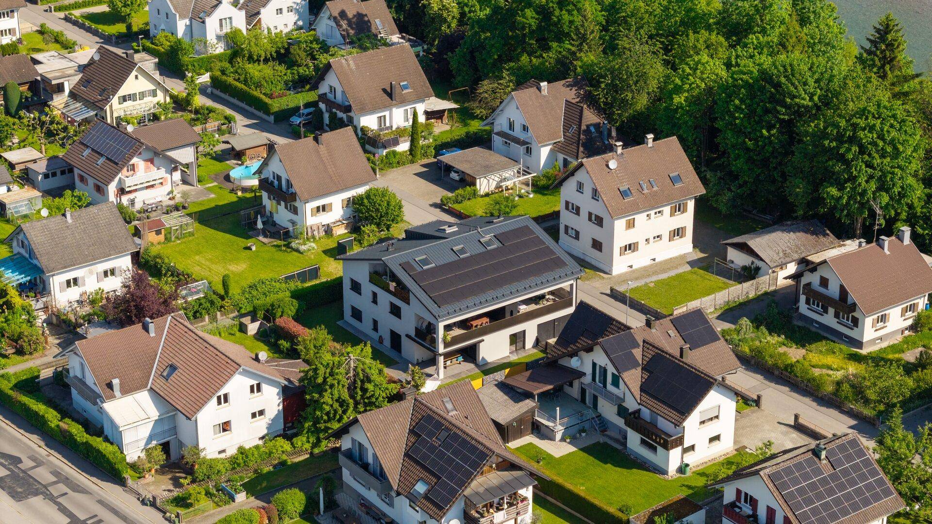 Luftaufnahme einer gepflegten Wohnsiedlung mit modernen Häusern, viel Grün und Solaranlagen auf den Dächern.