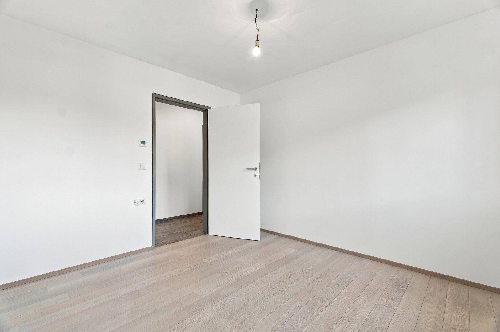 Geräumiges, unmöbliertes Schlafzimmer mit hellem Holzboden und offener Tür.