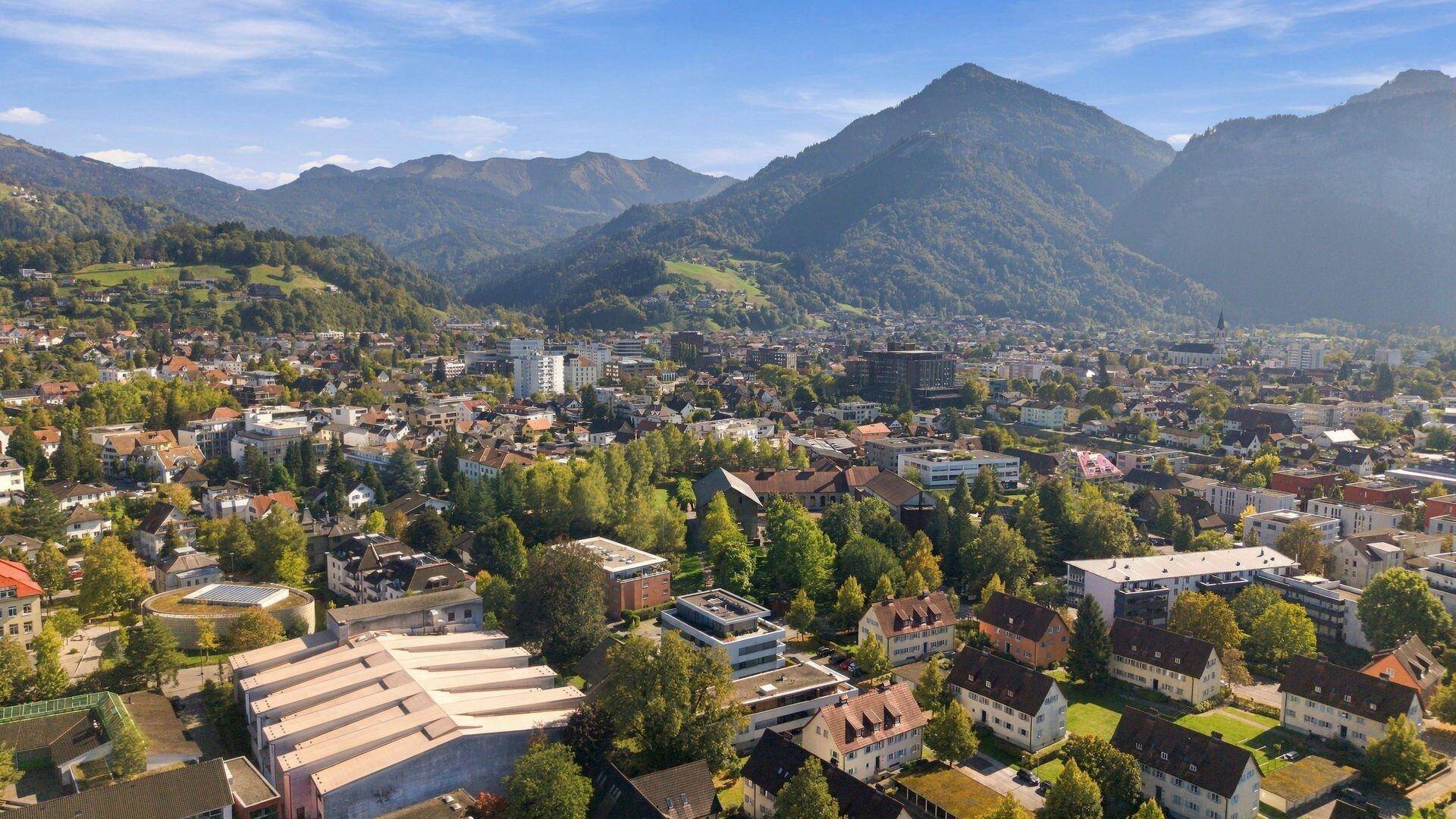 Malerischer Ausblick auf die Stadtlandschaft mit grünen Hügeln und Bergen am Horizont.