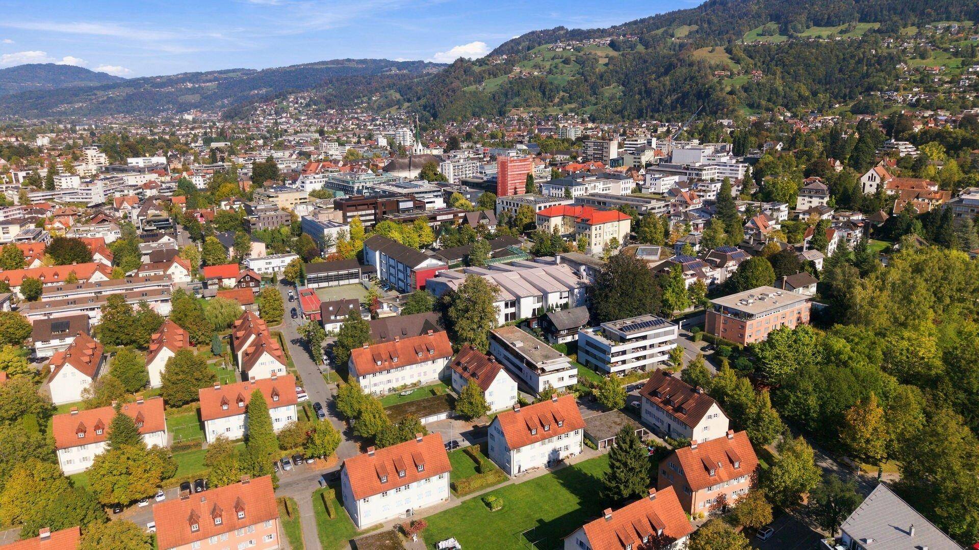 Panoramablick über eine Stadt mit Wohngebieten und Bergen im Hintergrund.