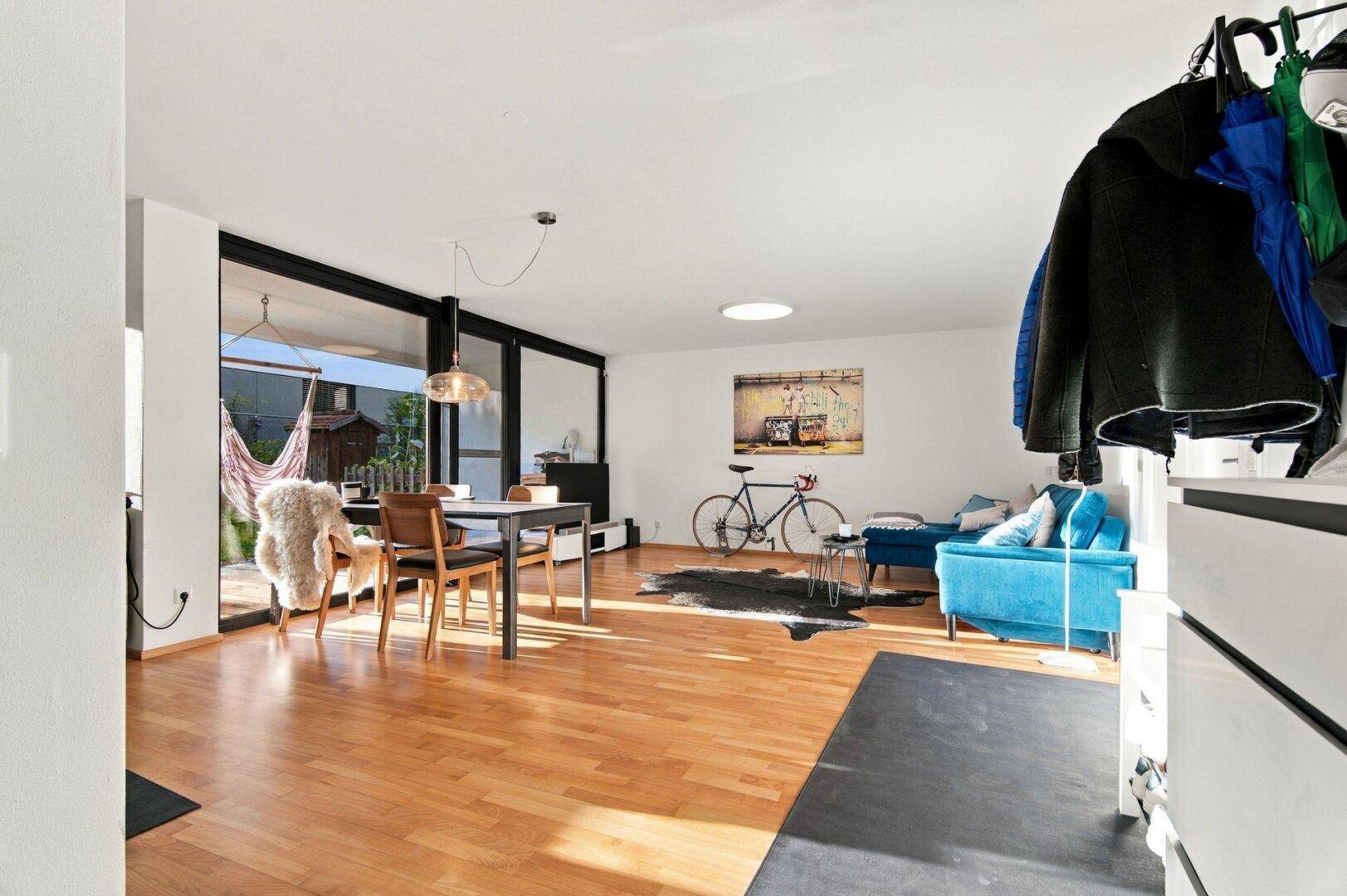 Geräumiger Wohn- und Essbereich mit Holzboden, blauer Couch und viel Tageslicht.