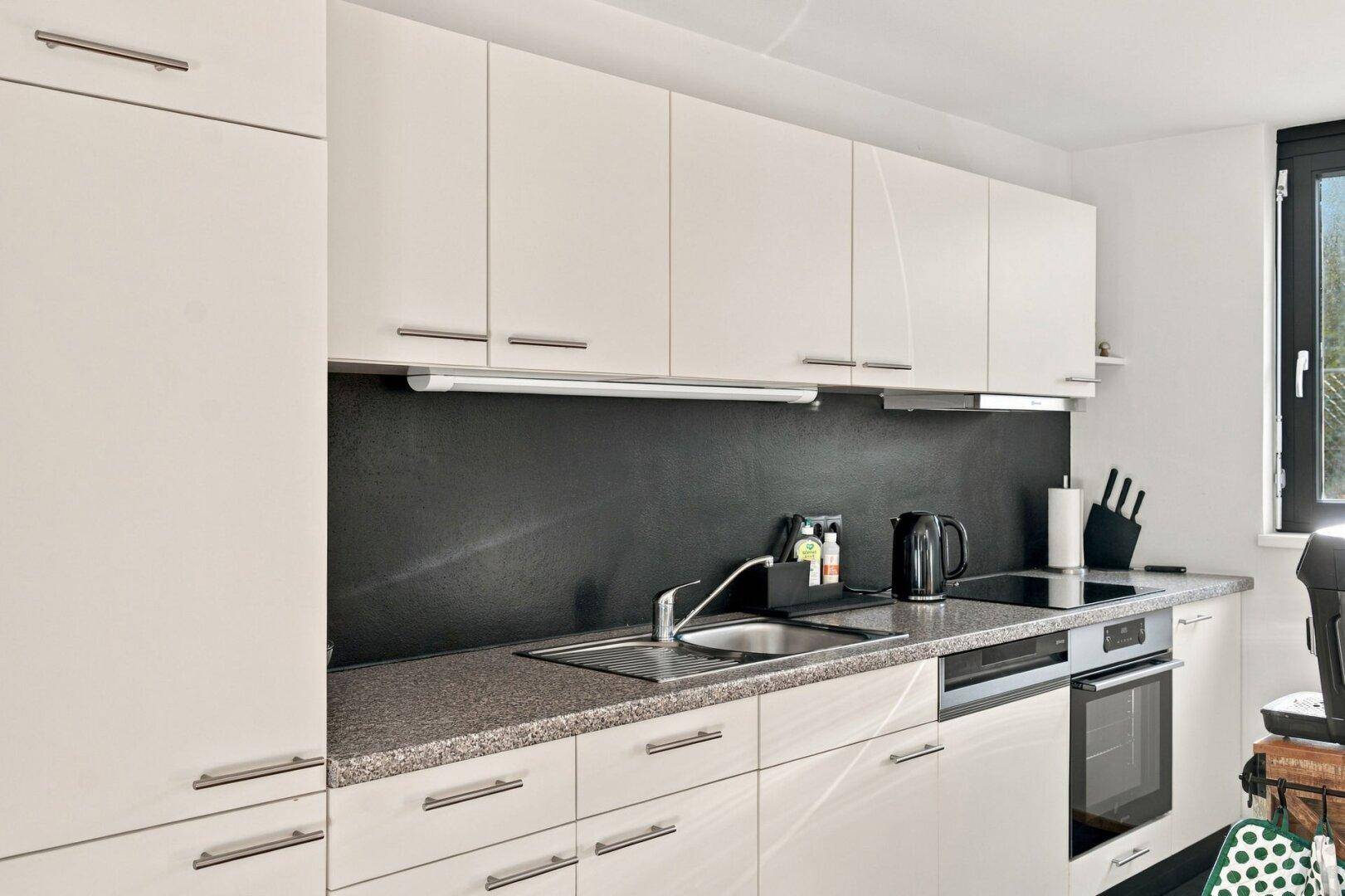Detailansicht der modernen Küche mit Spüle, Induktionskochfeld und Backofen.