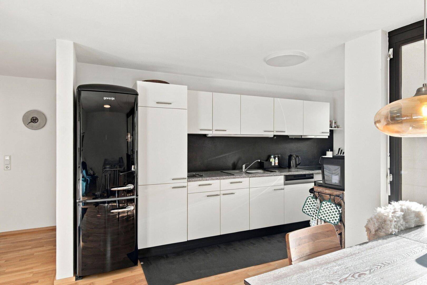 Helle Küche mit weißen Schränken, schwarzem Kühlschrank und Essbereich.
