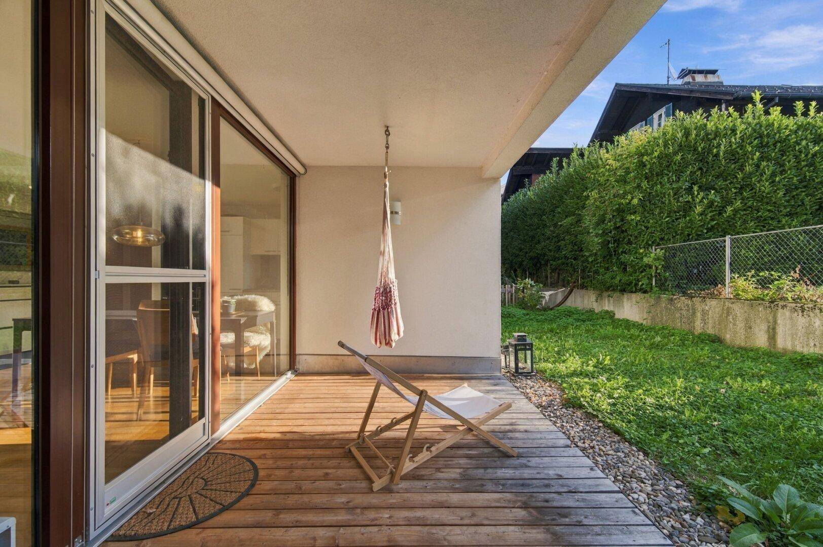 Geräumige Holzterrasse mit bequemen Gartenmöbeln, direktem Zugang zum Garten und Blick ins Grüne.