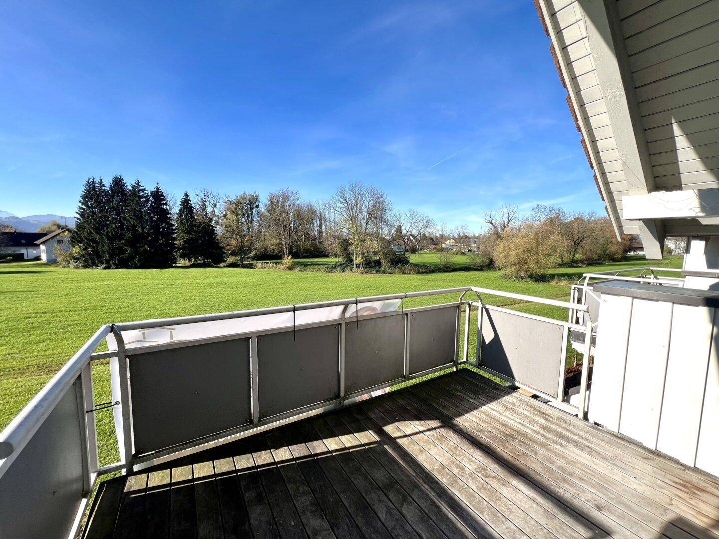 Geräumiger Balkon mit Holzboden und weitem Blick über grüne Felder und die umliegende Landschaft.